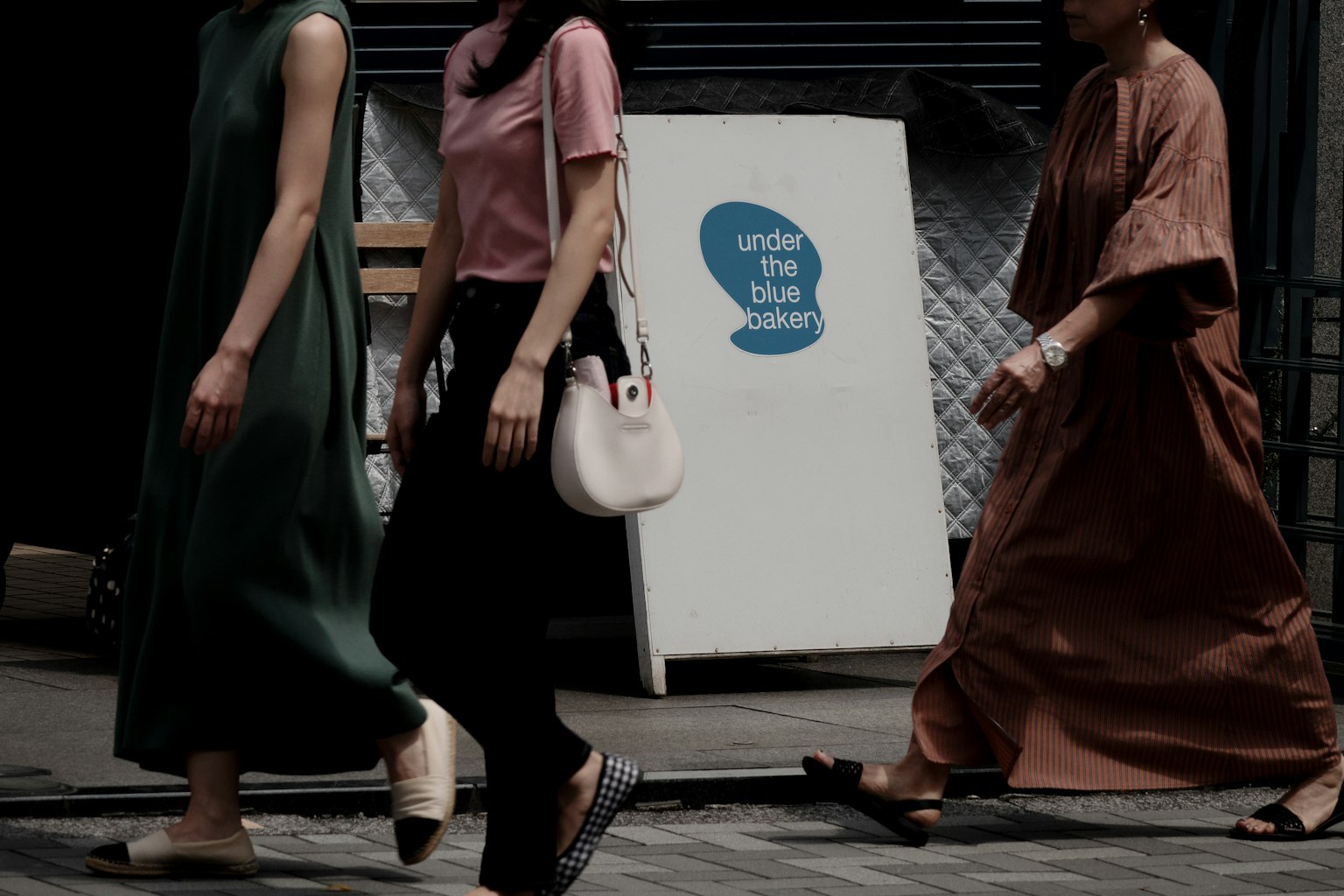 Women walking in an urban setting featuring modern fashion dresses and casual attire a white sign with a blue logo in the background