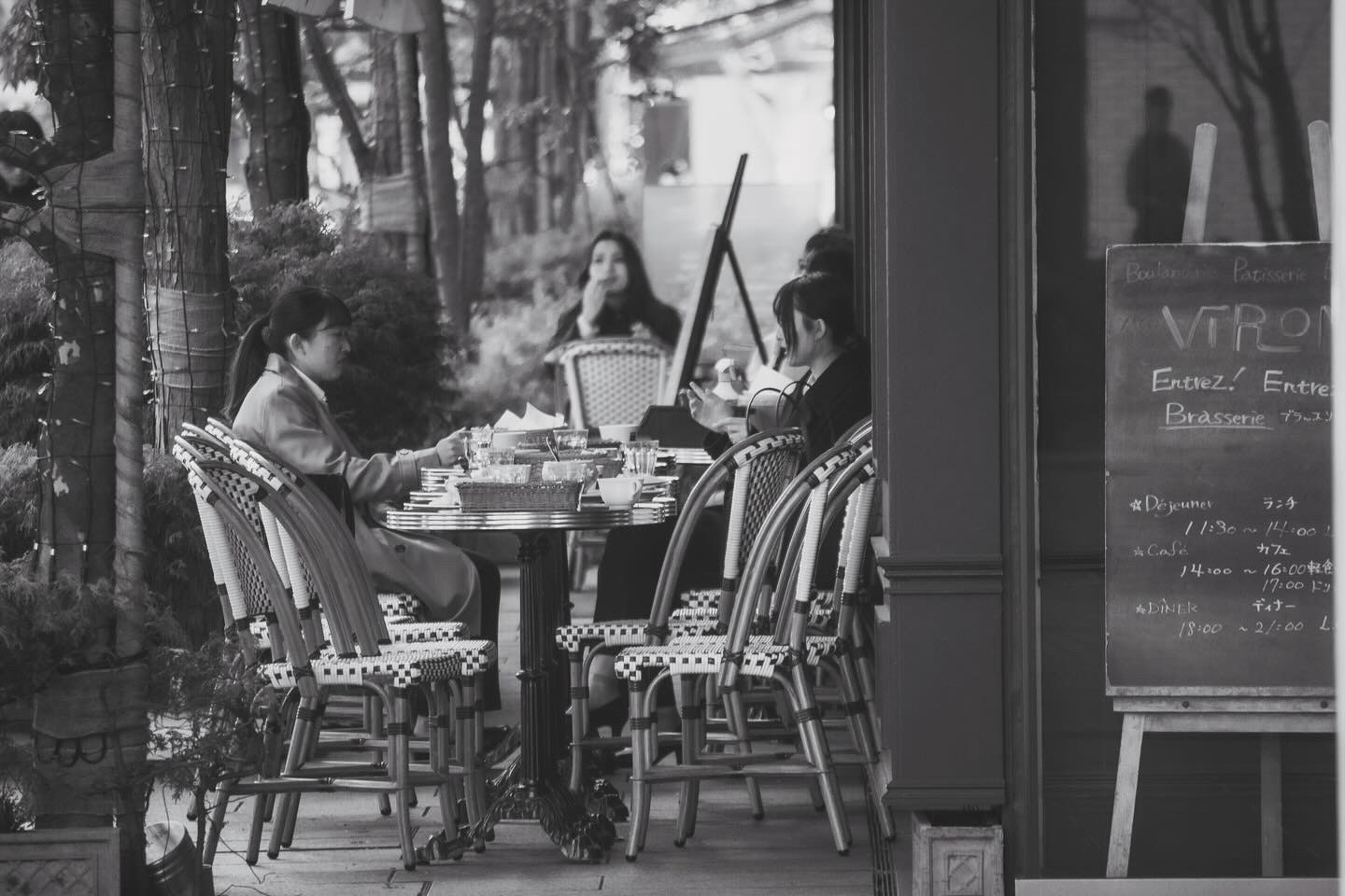 木々の並ぶテラスでテーブルを囲む人々の食事風景