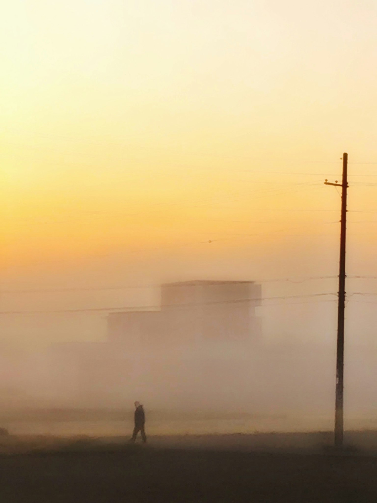 Silhouette di una persona che cammina nella nebbia con un edificio sullo sfondo