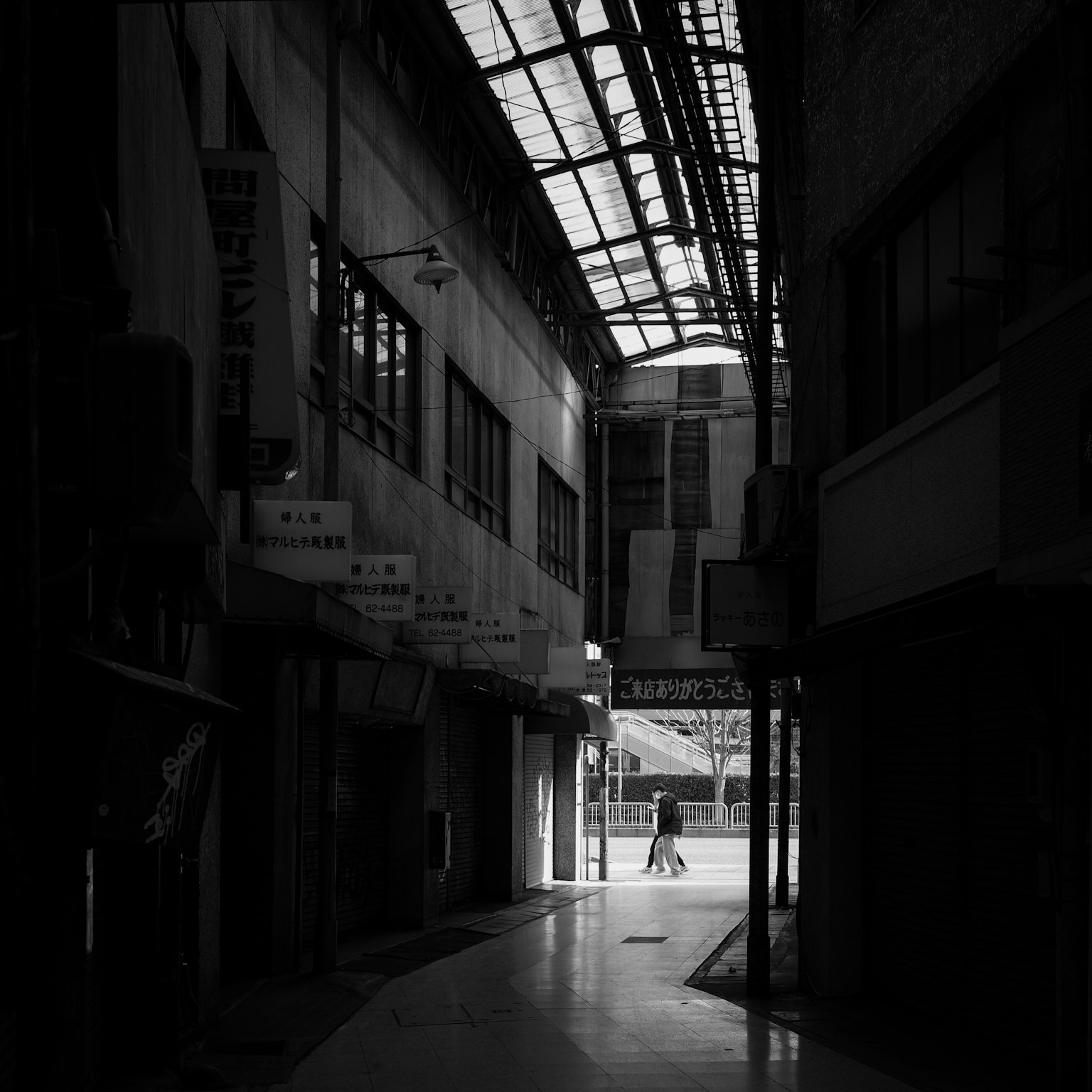 Black and white image of a person walking in a dimly lit alley