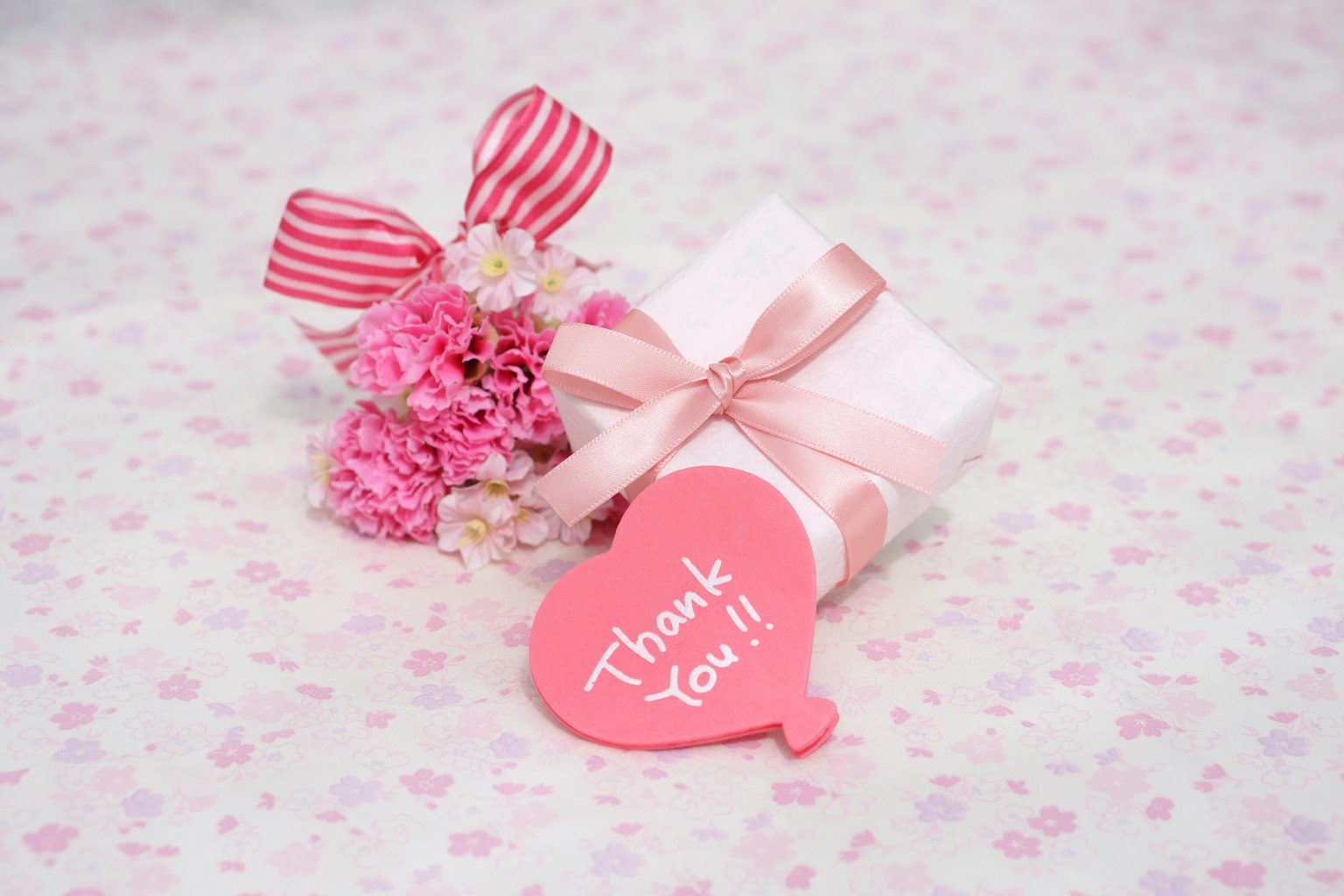 Scatola regalo con nastro rosa e bouquet di fiori, etichetta a forma di cuore con scritto Grazie