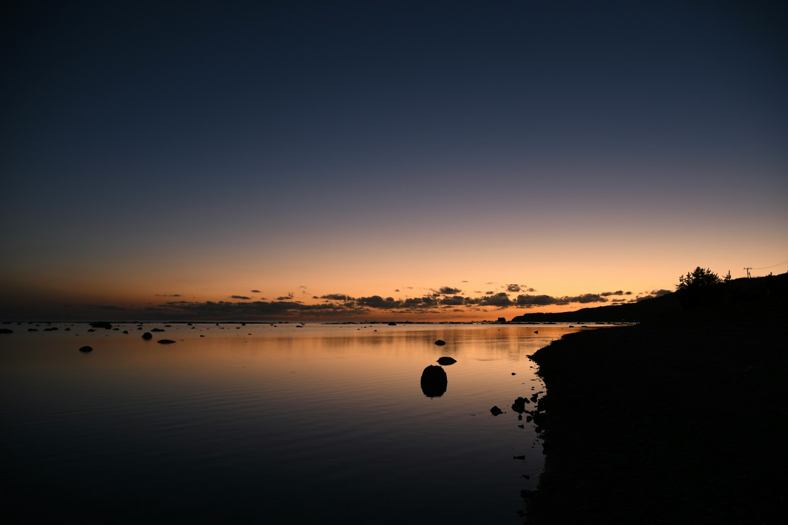 Lac tranquille au crépuscule avec une surface d'eau calme et un ciel crépusculaire présentant des rochers le long de la rive