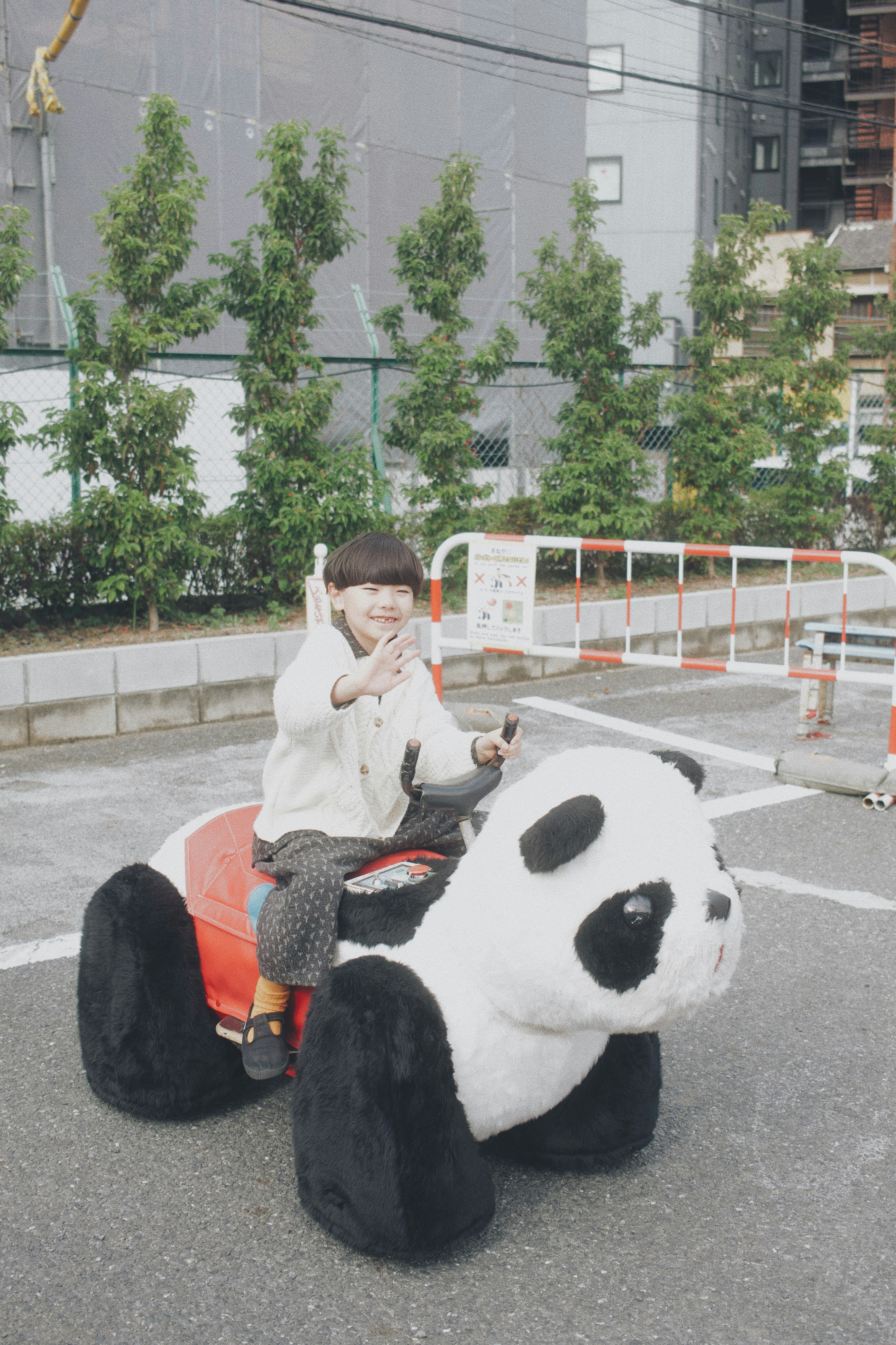 Child waving while sitting on a panda ride in an outdoor play area