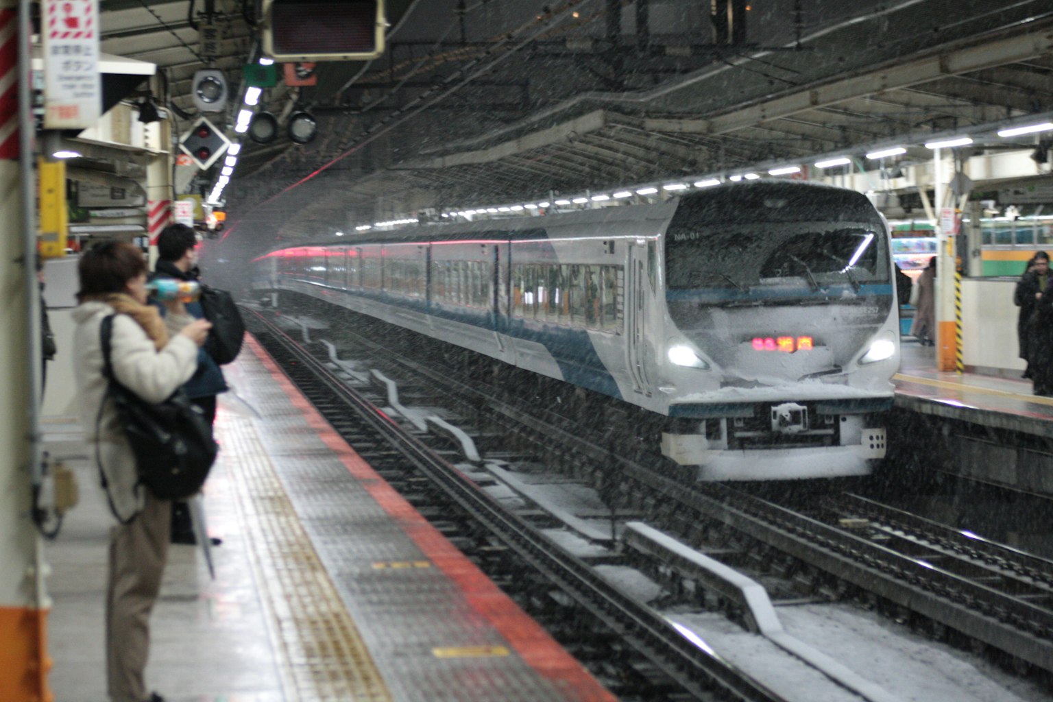 Treno moderno in arrivo a una stazione sotto la pioggia con passeggeri in attesa