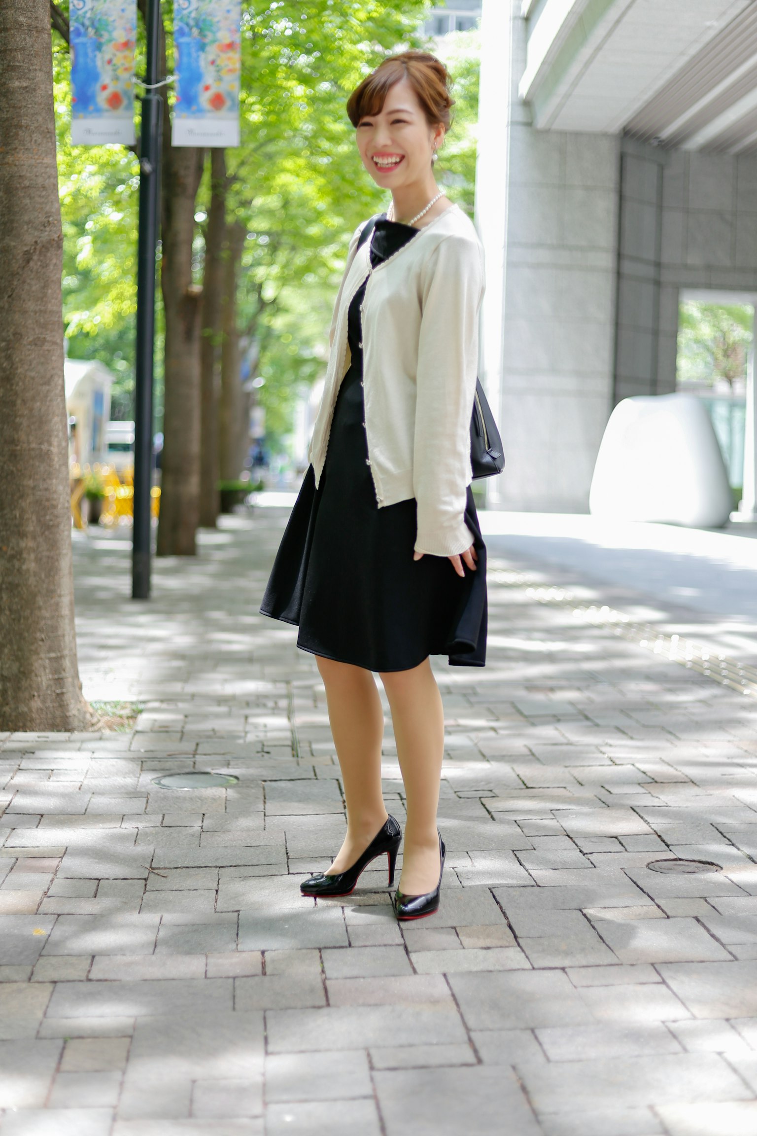Une femme portant une robe noire et un cardigan blanc marchant dans une rue de la ville