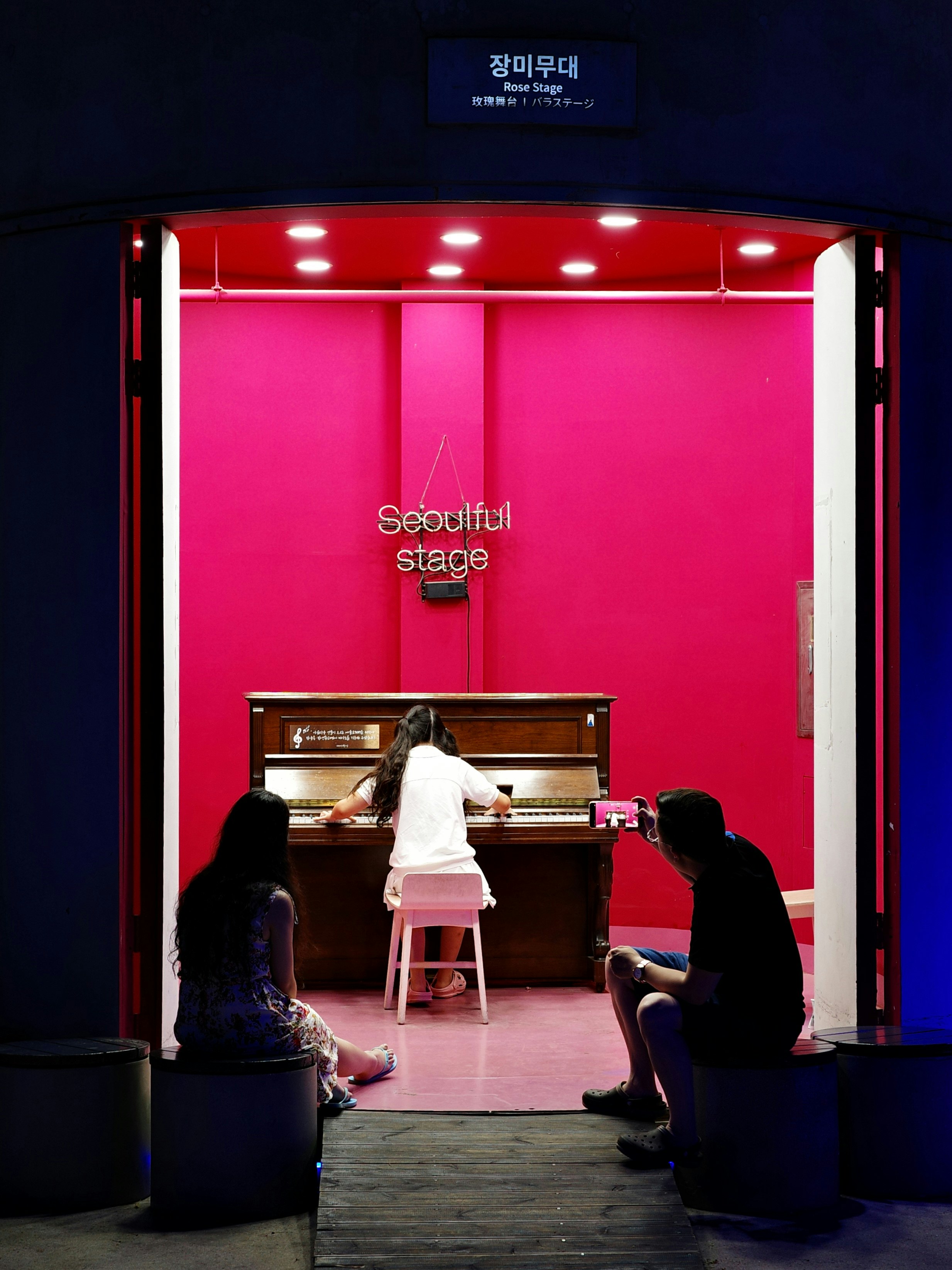 một người đang chơi piano trên sân khấu nhỏ với phông nền màu đỏ