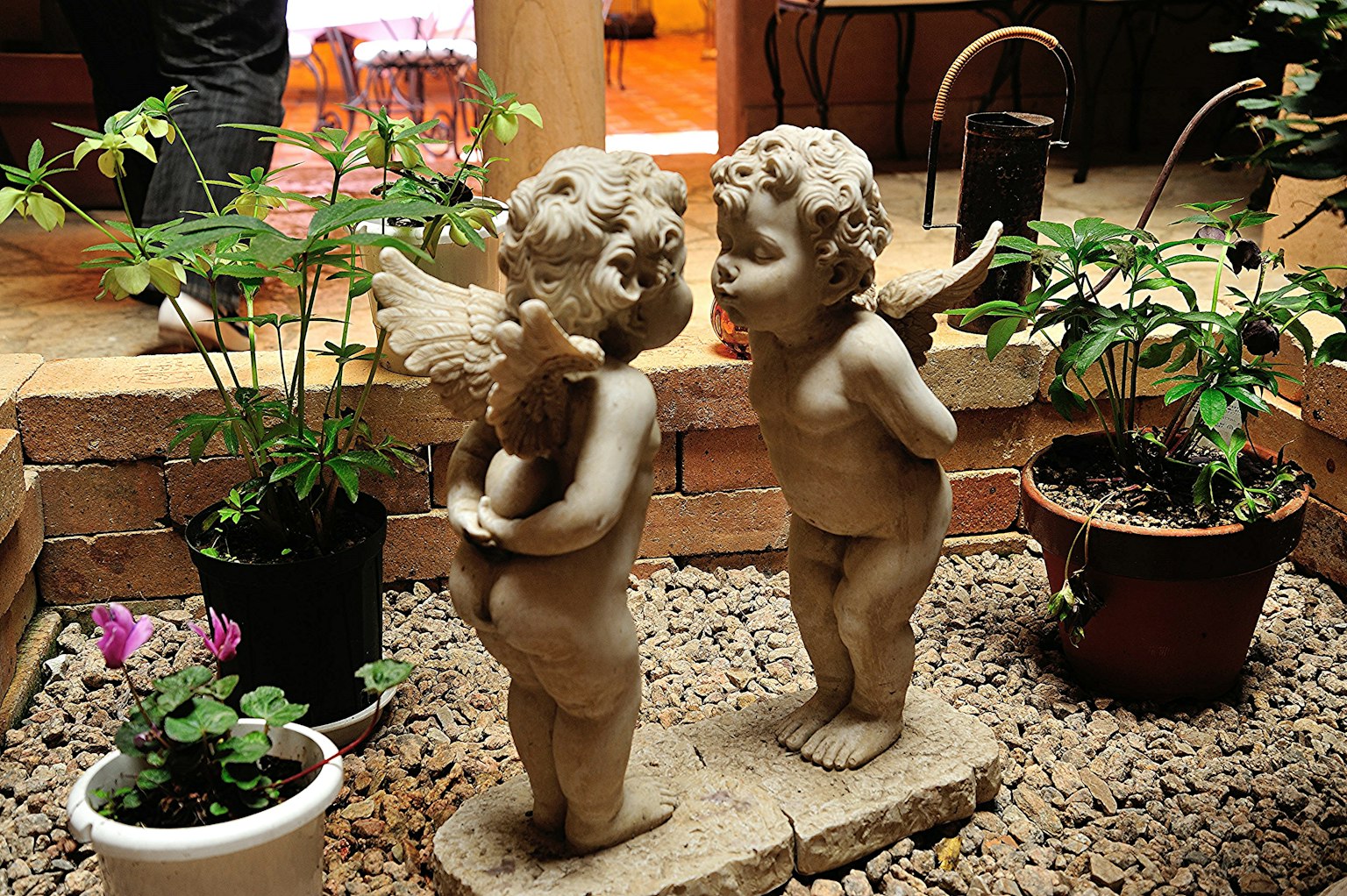 Due statue di cherubini in un giardino circondate da piante