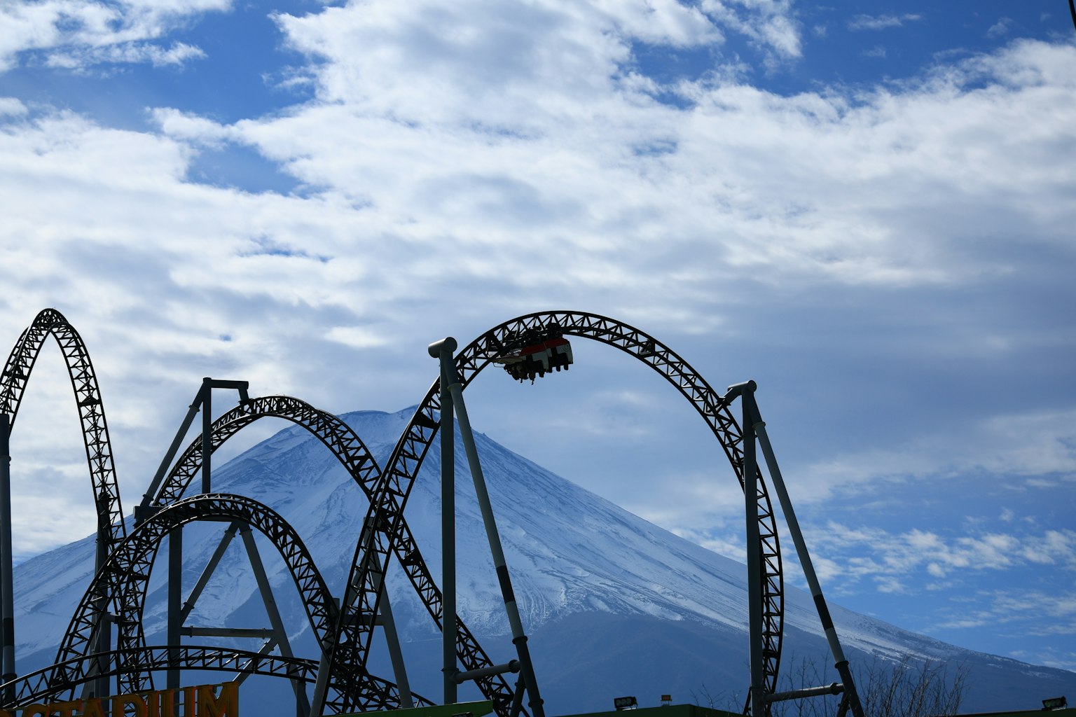 Roller coaster attraction with Mount Fuji in the background under a partly cloudy sky