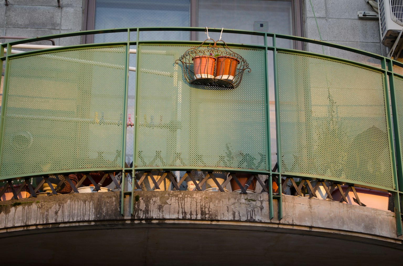 Un balcon verde con un vaso di legno appeso e pannelli trasparenti