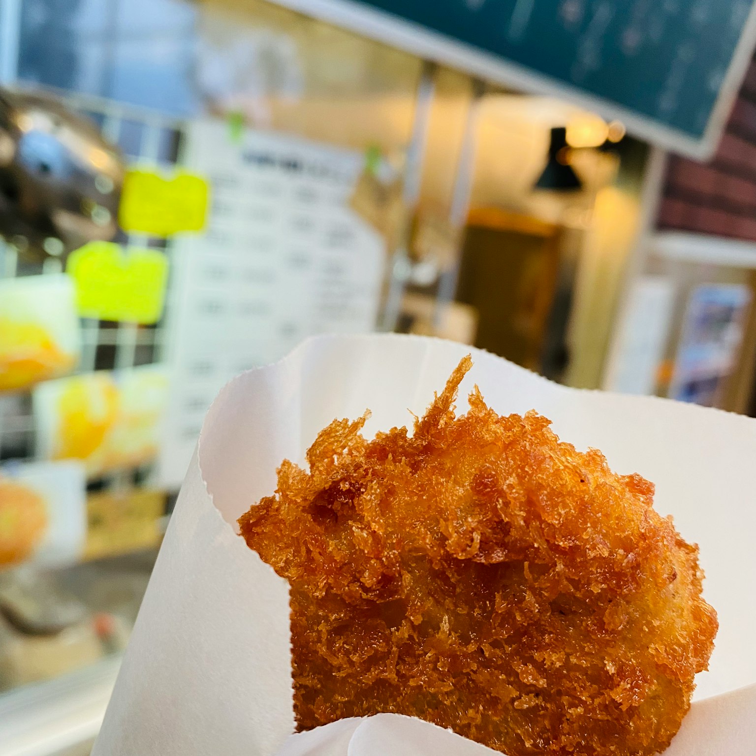 Crocchetta appena fritta avvolta in carta bianca con un menu visibile sullo sfondo