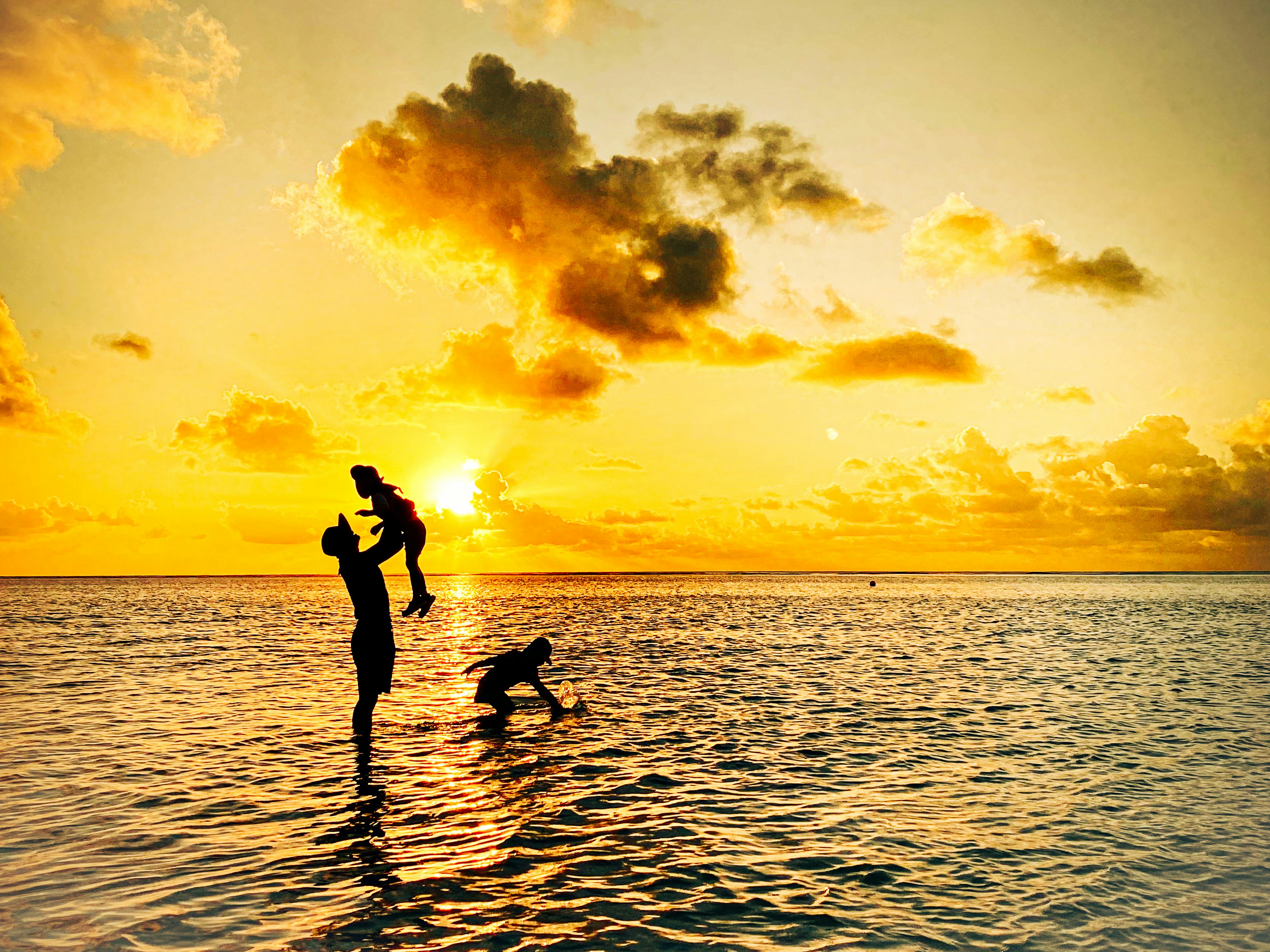 夕日に照らされた海辺で遊ぶ親子のシルエット