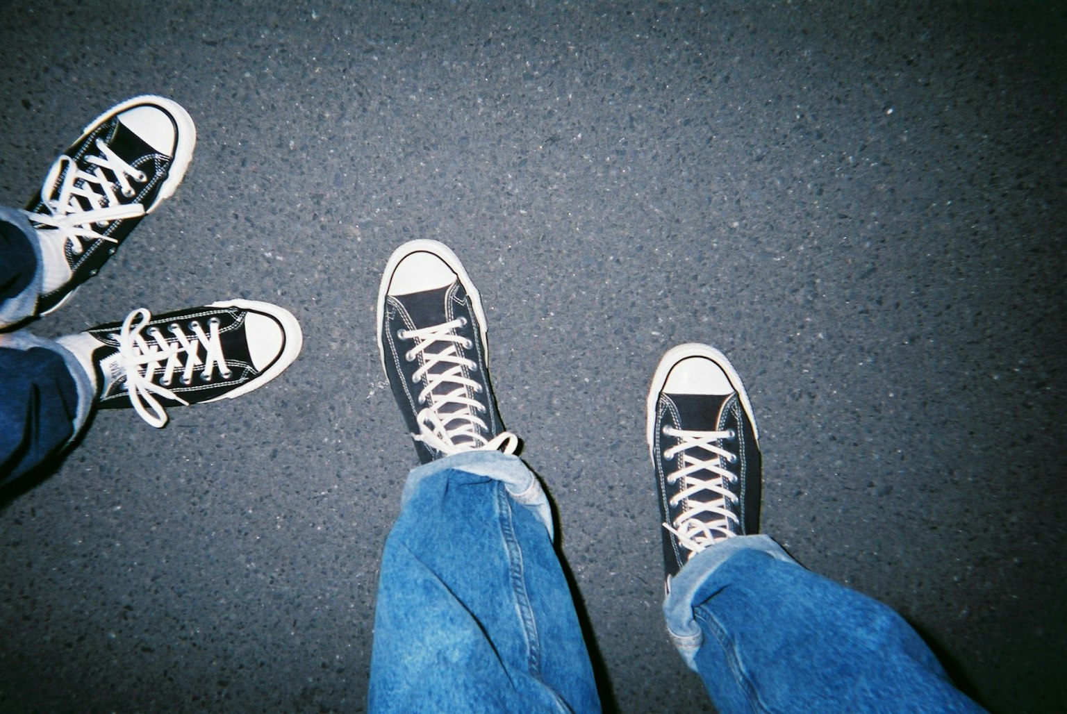 Une photo de deux paires de pieds portant des baskets Converse noires sur une surface sombre