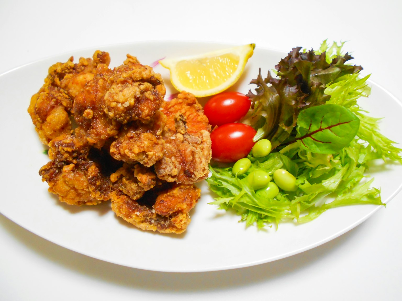 Pollo frito servido en un plato blanco con ensalada fresca y limón
