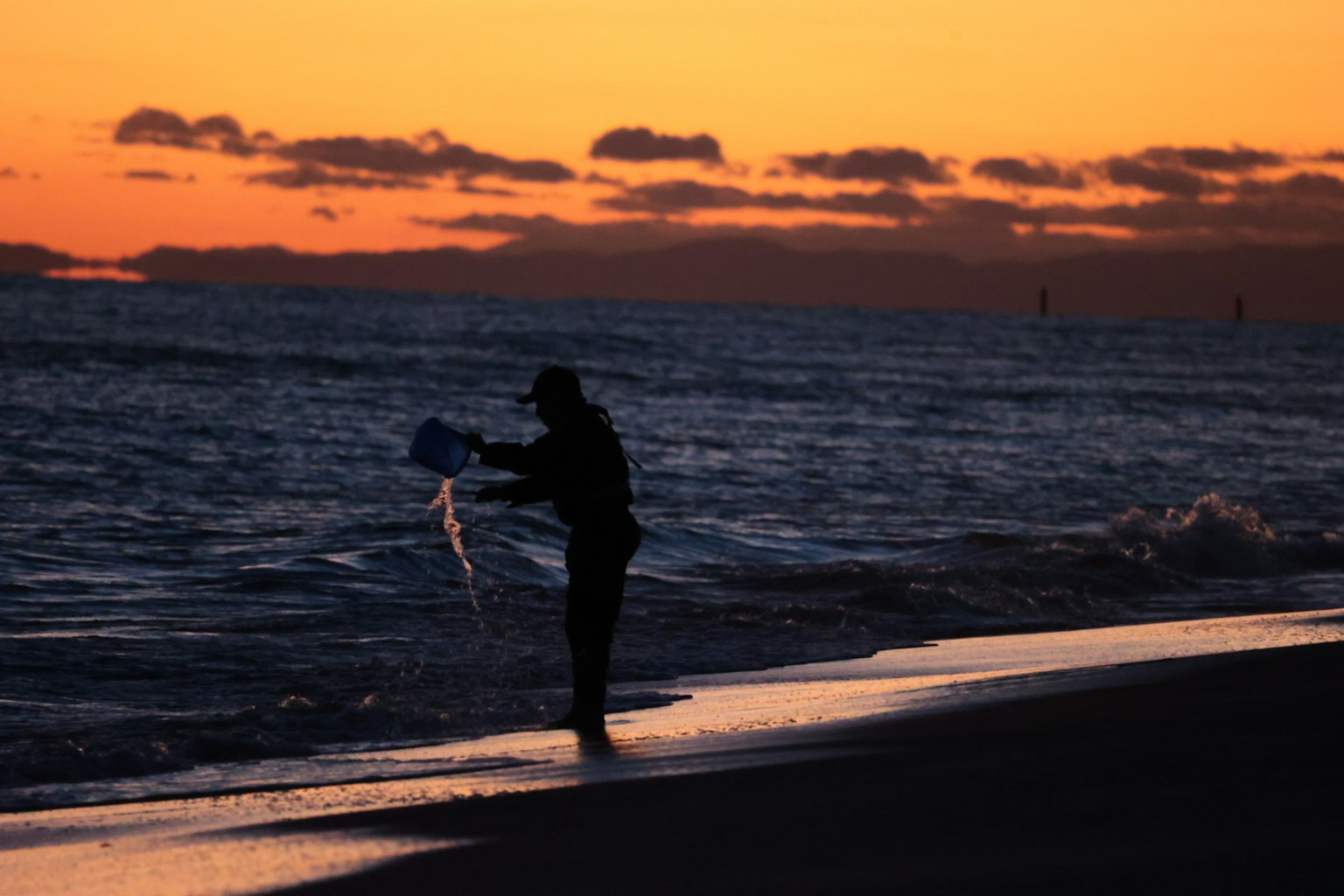 Silhouette di una persona che tiene un aquilone al tramonto vicino all'oceano
