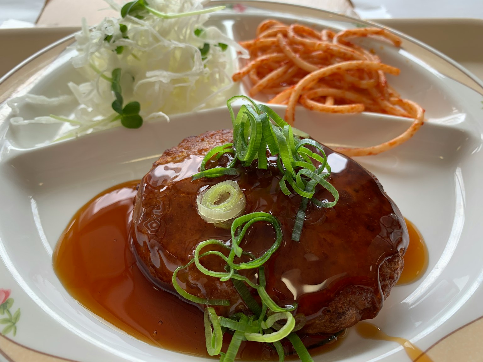 Immagine di un hamburger guarnito con cipollotti e salsa teriyaki servito con insalata e noodles croccanti