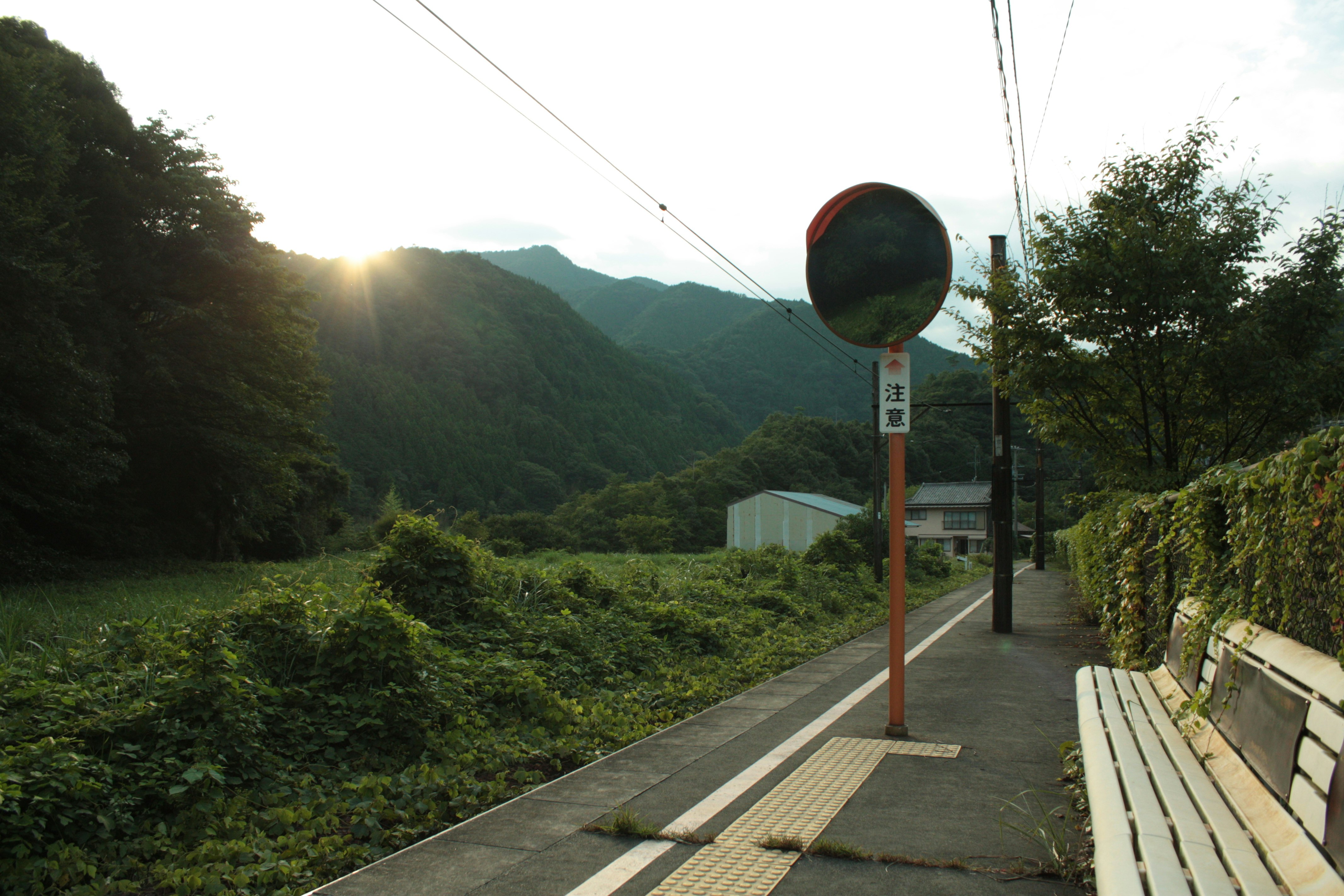 山あいの田舎道と夕方の街灯、停留所の標識のある風景