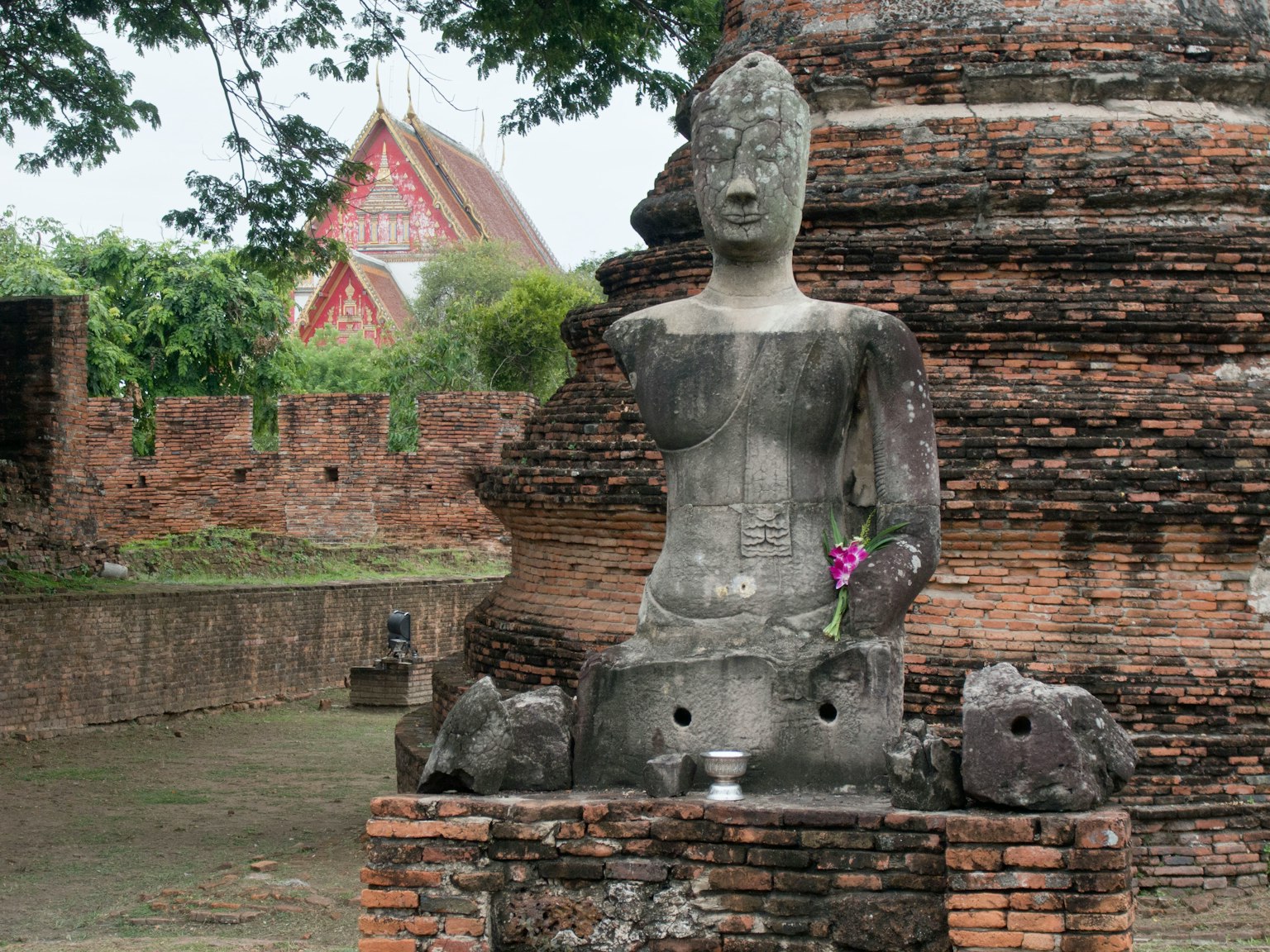 Patung Buddha kuno di dekat reruntuhan bata dengan persembahan bunga
