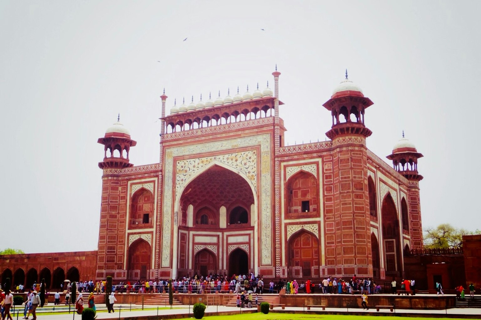 Entrance of the Taj Mahal featuring red brick architecture and arches with many tourists
