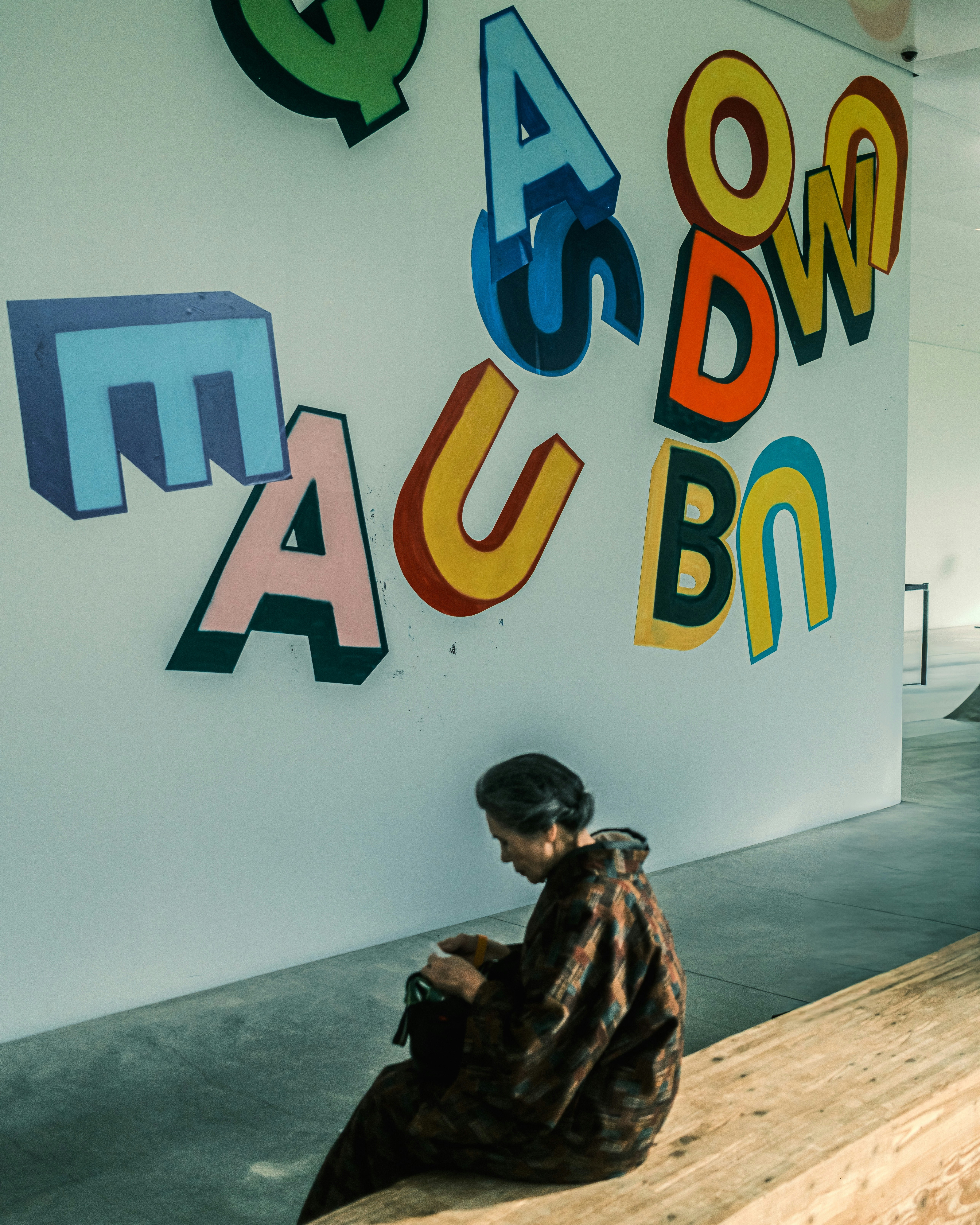 texto tipográfico colorido en una pared con una persona sentada en un espacio de exposición