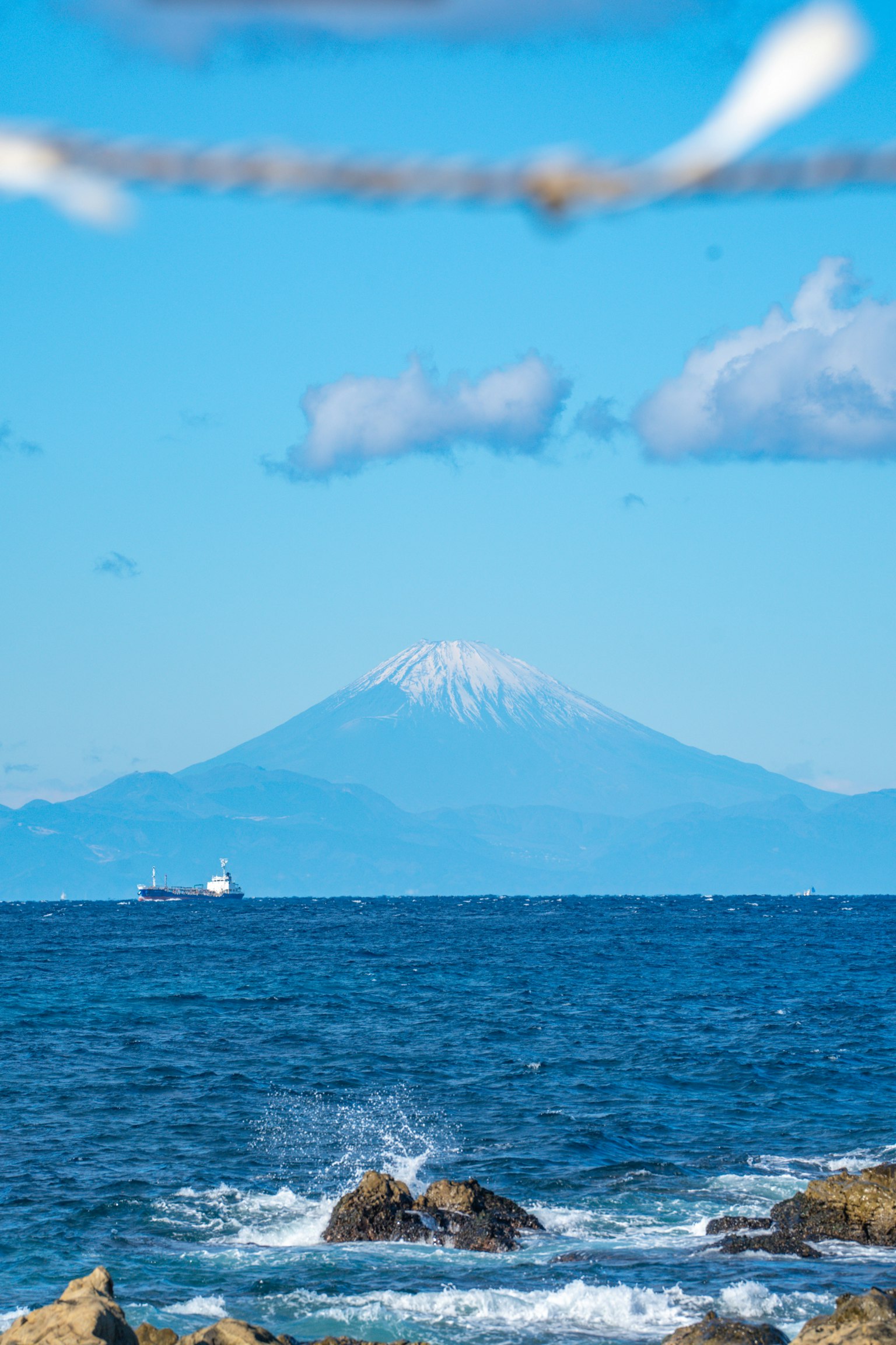 Una montagna innevata sullo sfondo con mare blu e nuvole bianche