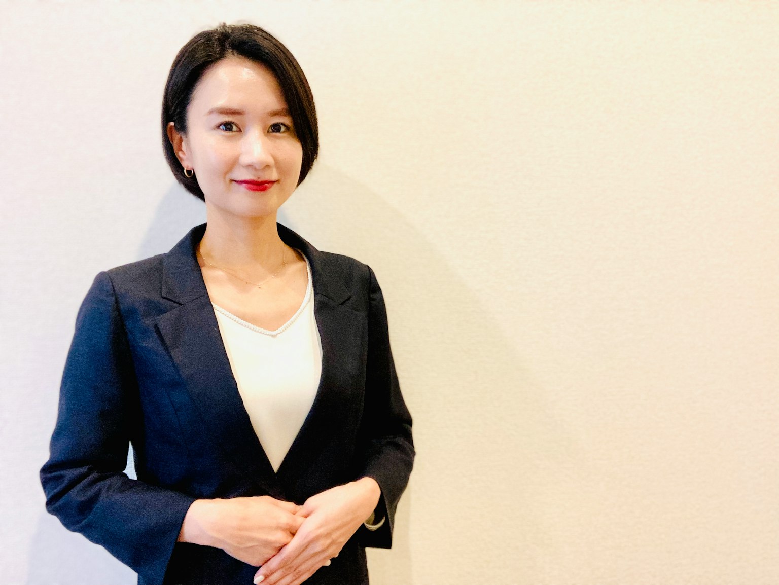 정장을 입은 여성이 밝은 배경 앞에서 미소를 지으며 서 있다