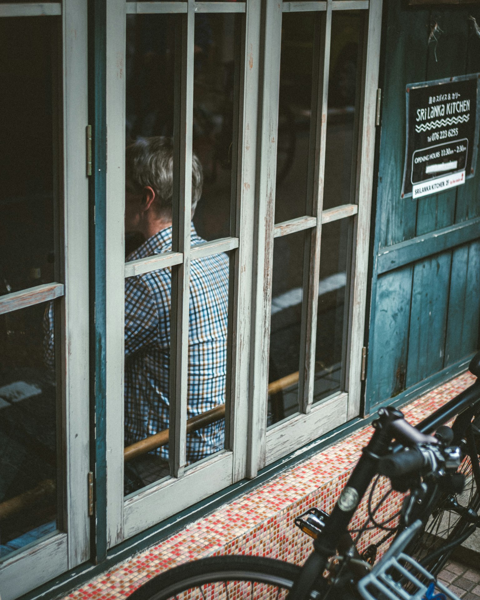 Seorang pria duduk di belakang pintu kayu biru dengan sepeda diparkir di dekatnya