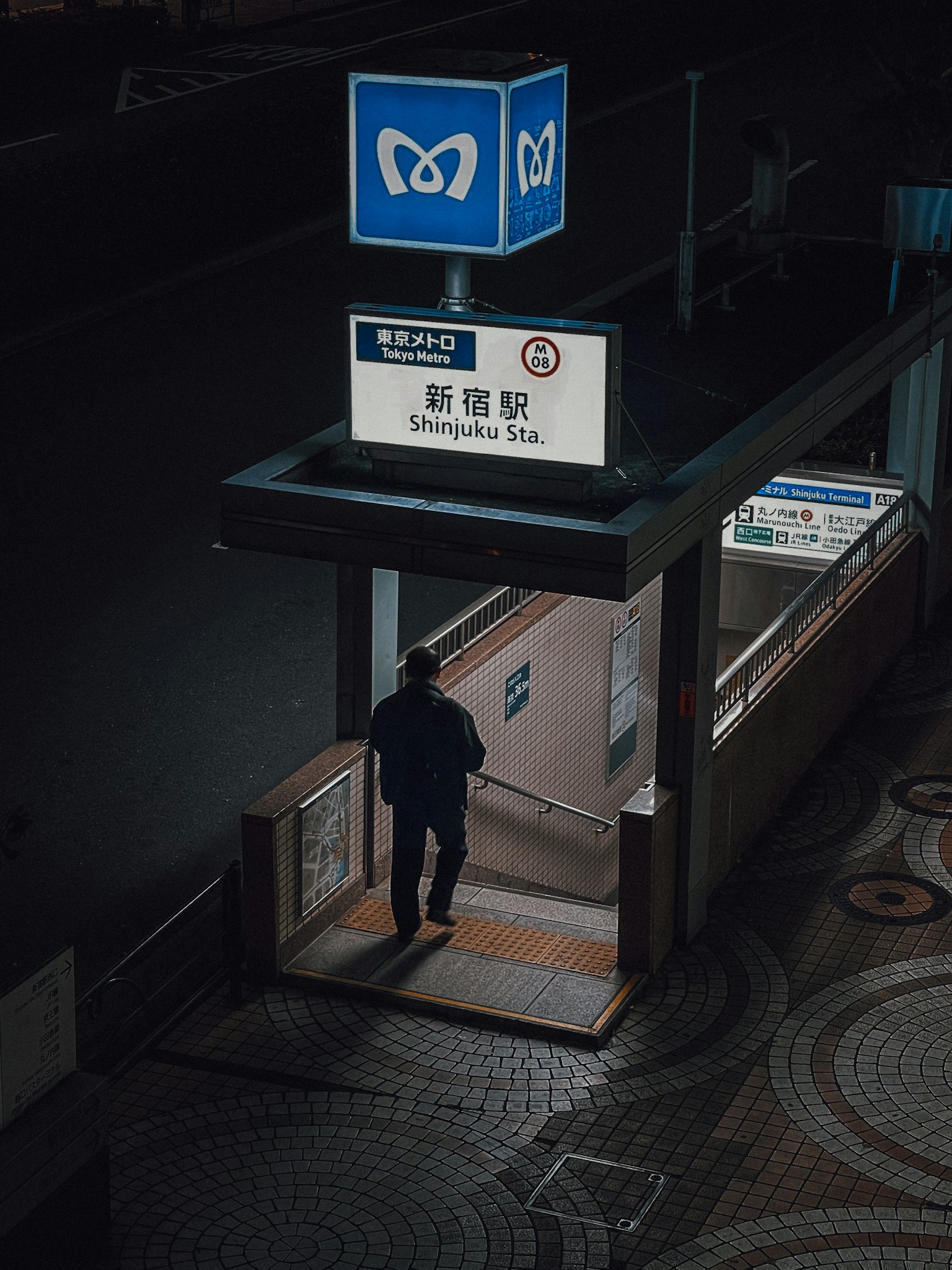Un uomo in piedi all'ingresso di una stazione della metropolitana di notte con un segnale blu