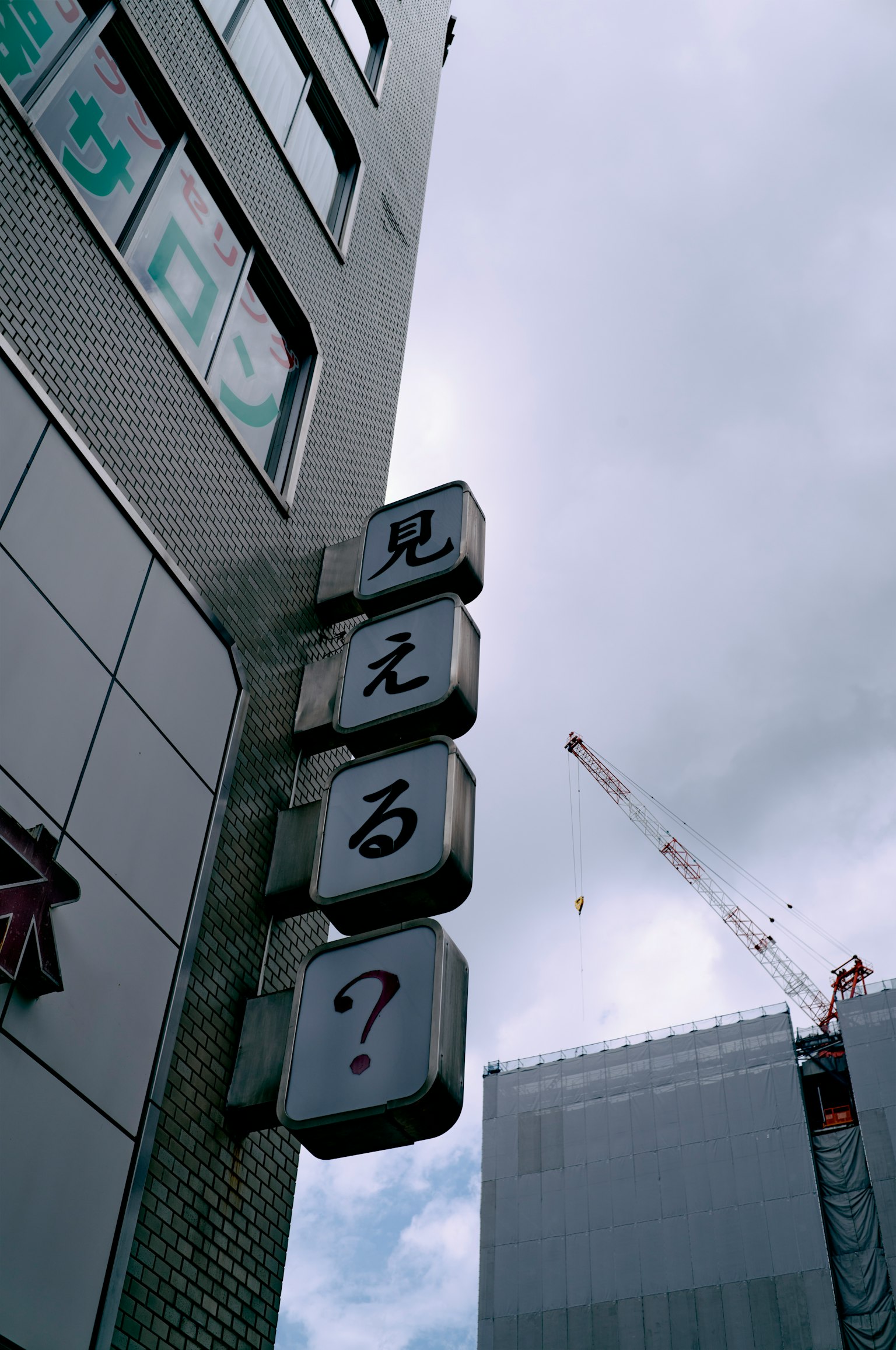 Corner of a high-rise building featuring an unknown sign and cloudy sky