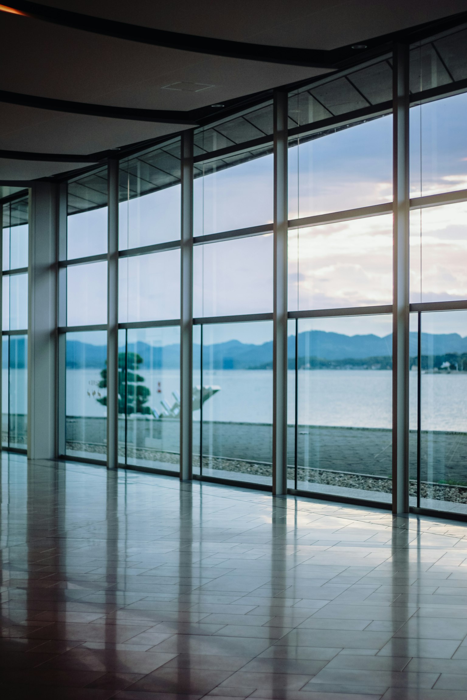 Interior moderno con grandes ventanas de vidrio que muestran una vista de un lago y montañas
