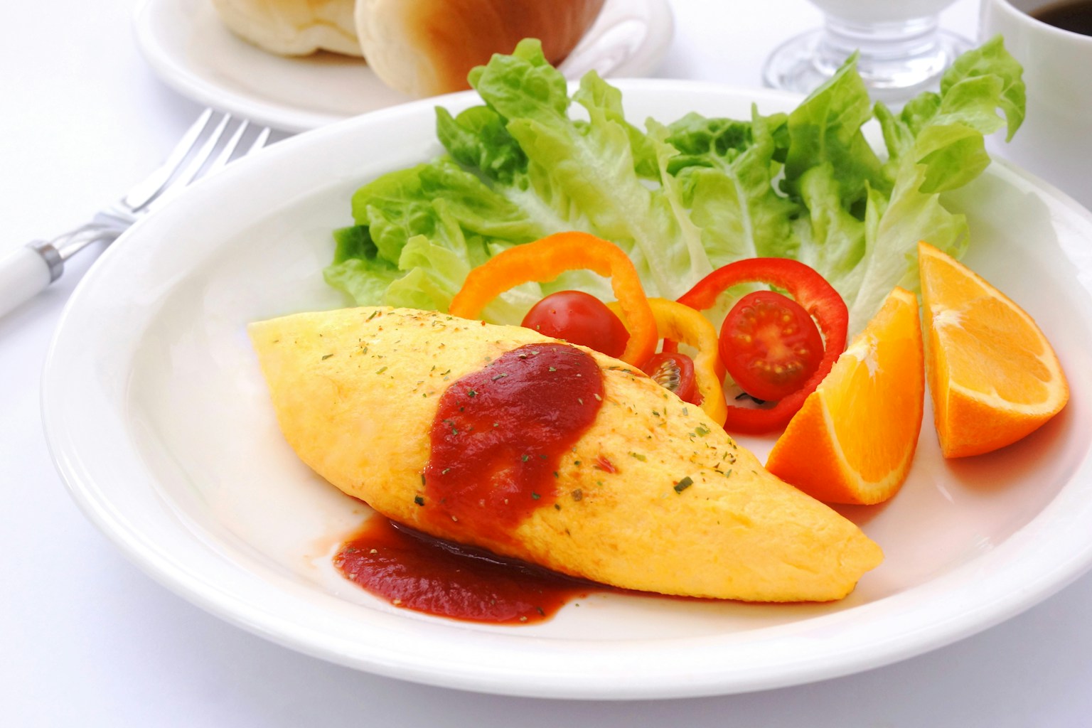 Ein Teller mit Omelette mit Sauce, frischem Salat, Tomatenscheiben und Orangenspalten