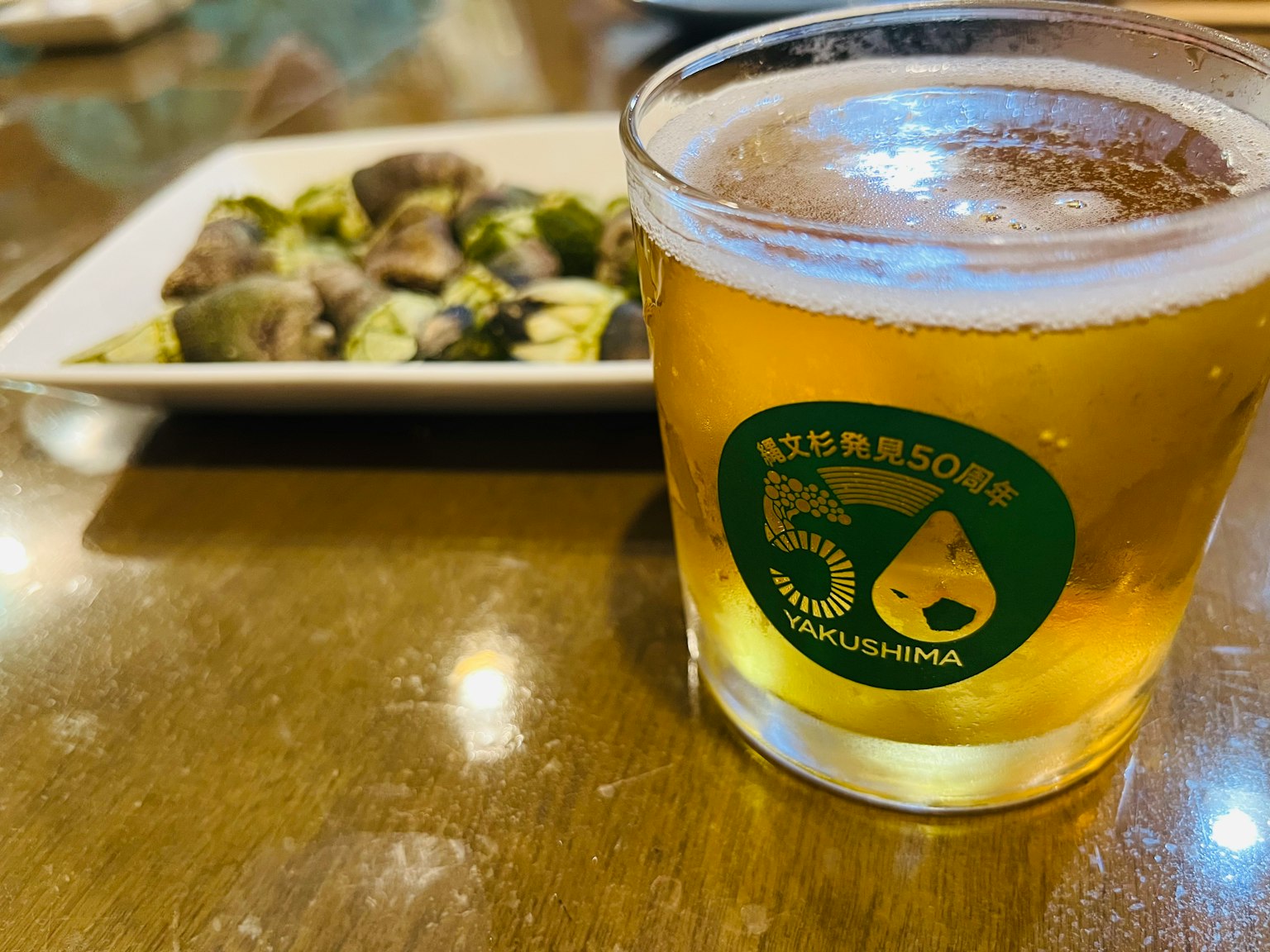 A glass of beer next to a plate of shellfish on a wooden table