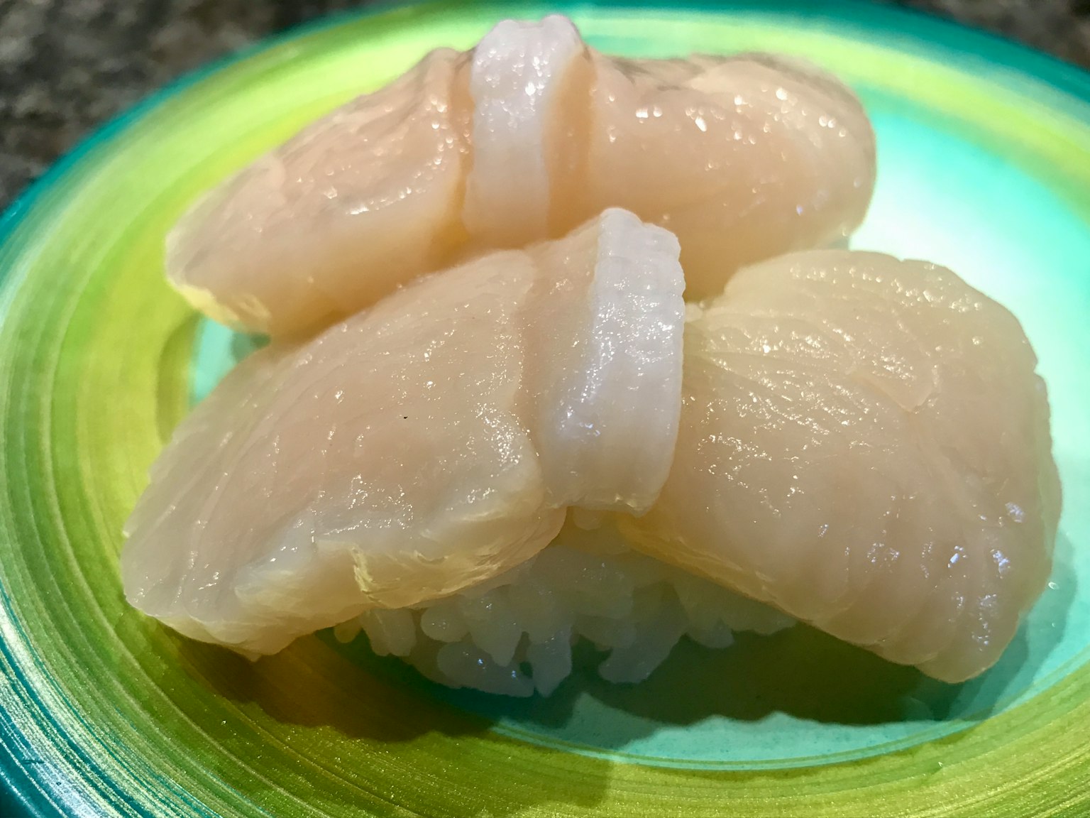 Scallop nigiri sushi served on a vibrant green plate