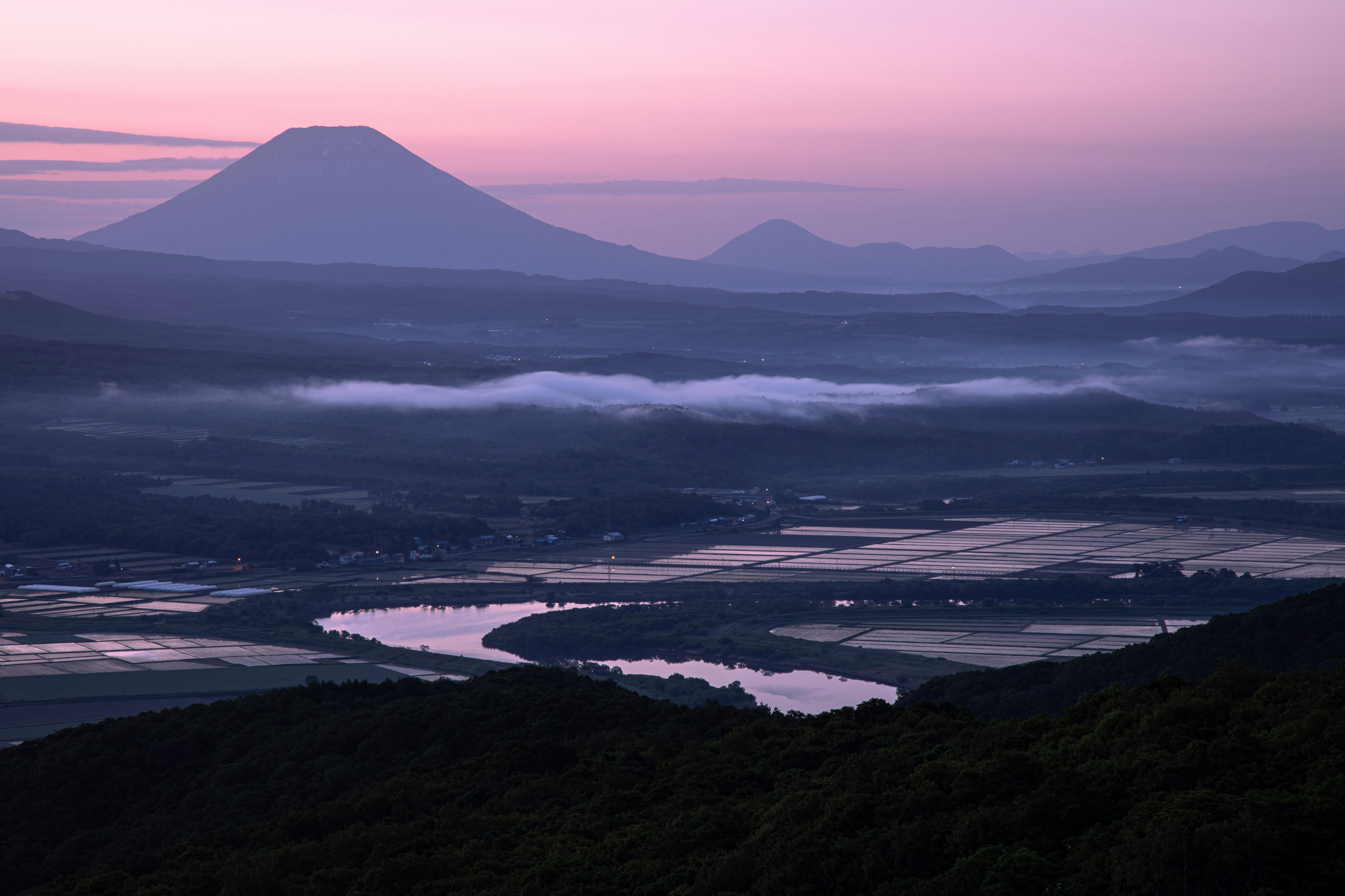 霧のかかった川と田園、遠くに山並みが重なる夕景