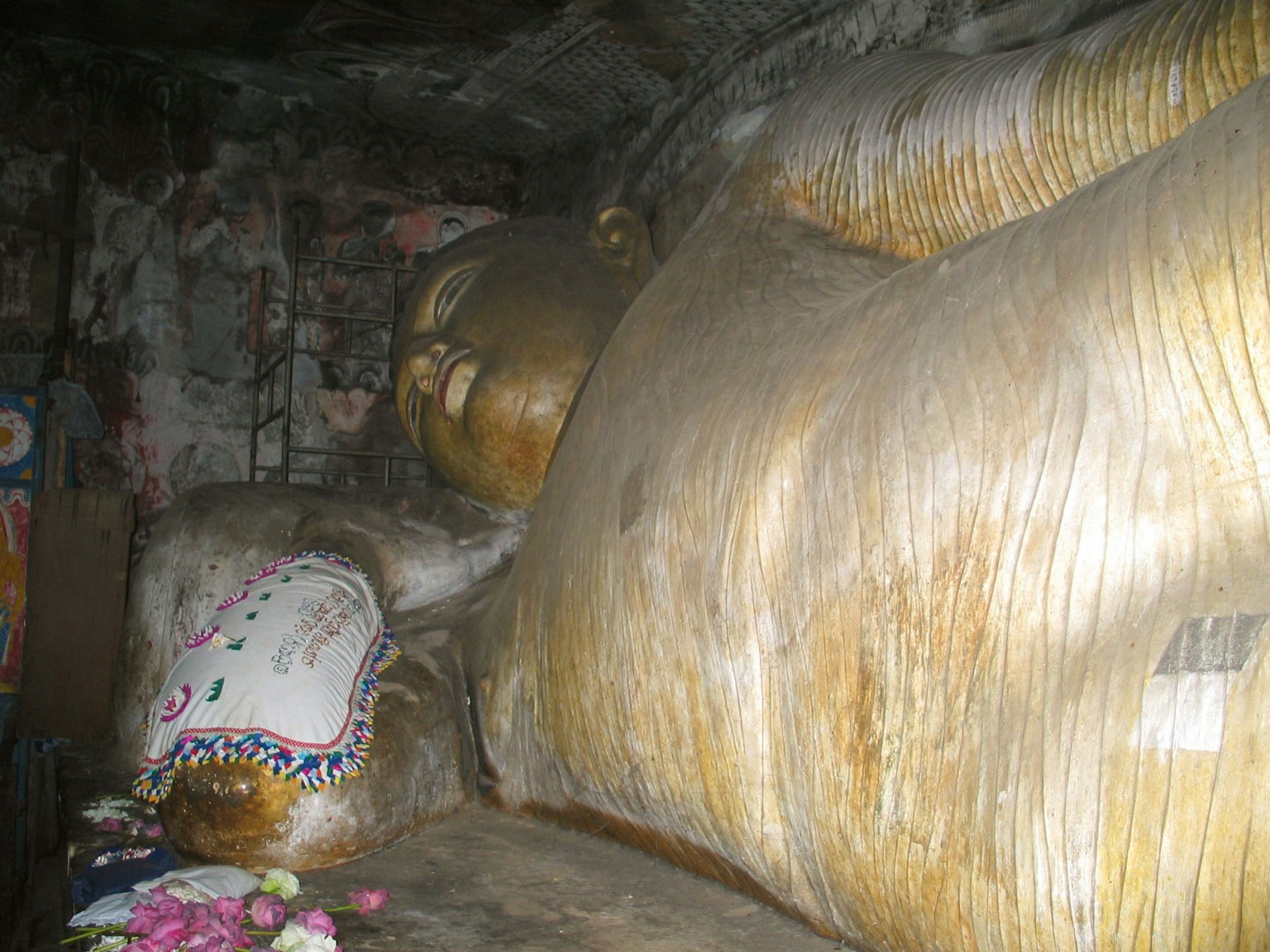 Image of a large reclining Buddha statue inside a cave with golden skin and a decorated pillow
