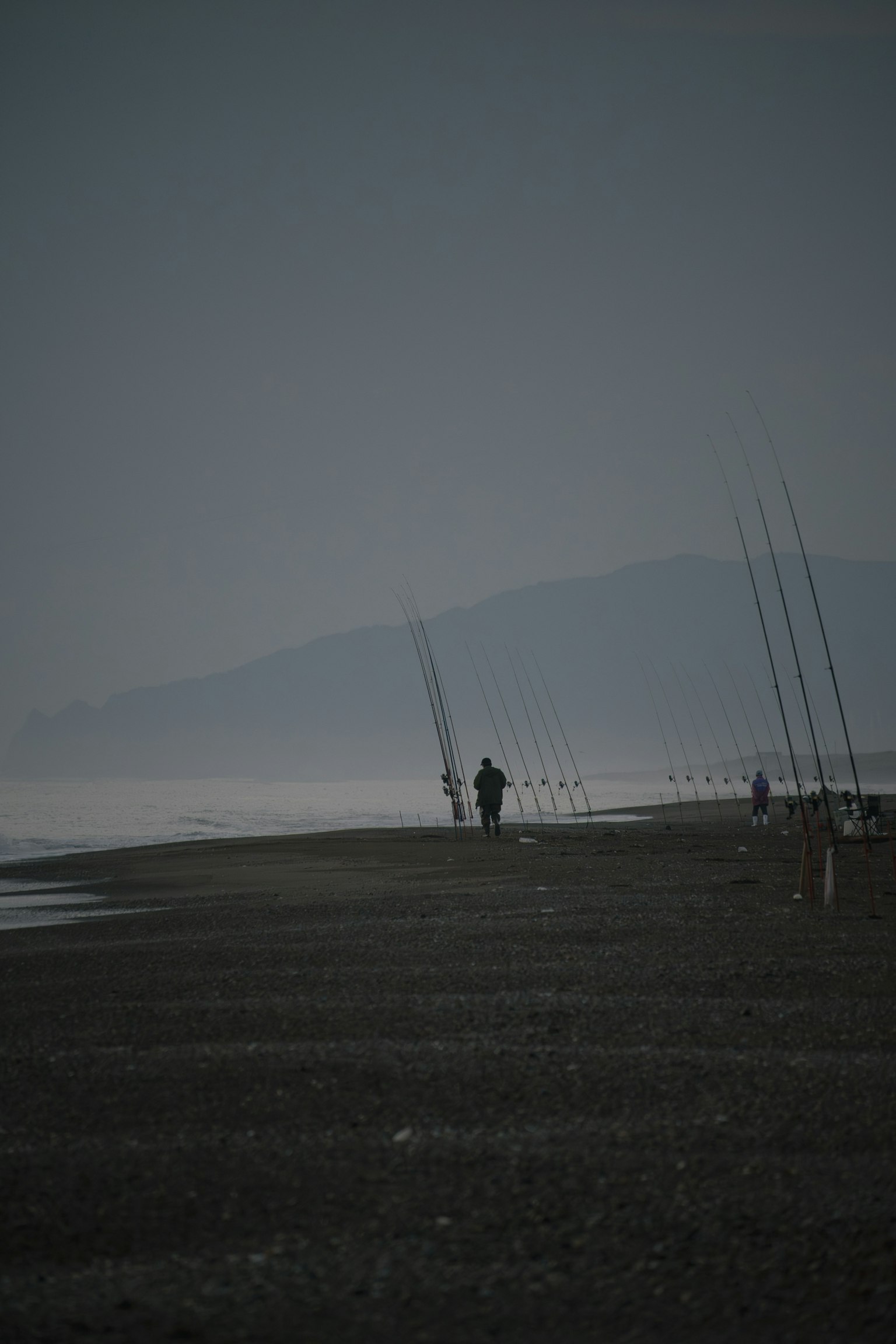 Silhouette d'une personne pêchant sur une plage tranquille avec des montagnes au loin