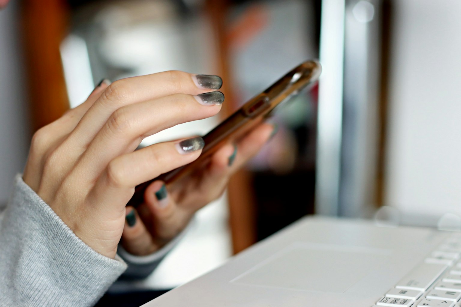 Une main tenant un smartphone à côté d'un clavier d'ordinateur portable