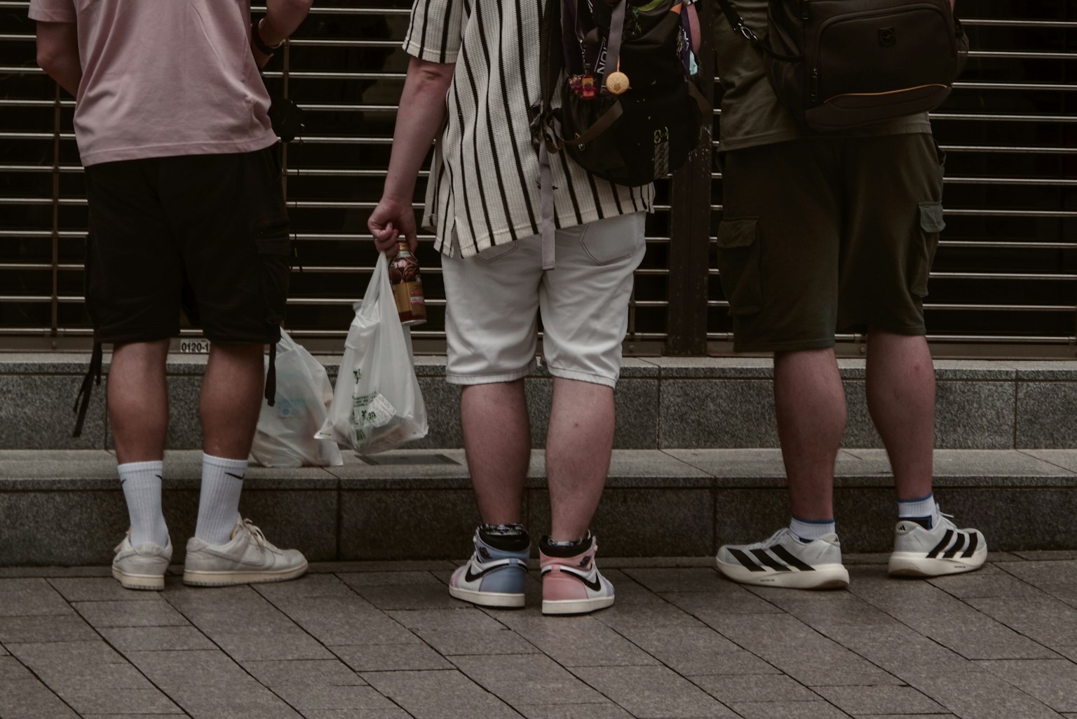 三名男子背对着站着 穿着短裤和运动鞋 一人手持购物袋