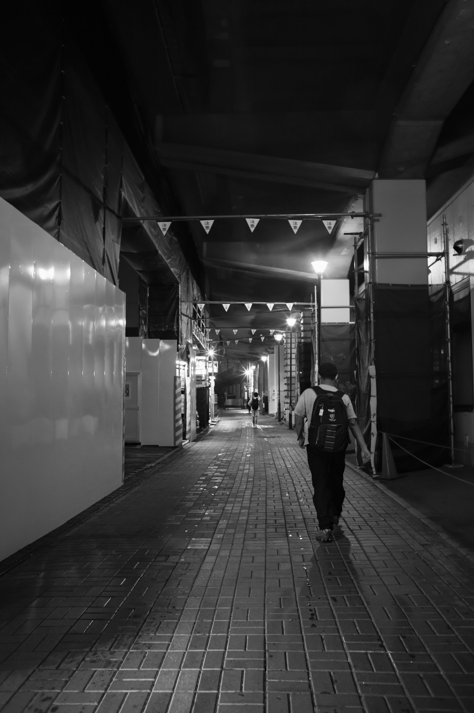 一個人在黑白小巷中行走，散落的燈光和陰暗的氛圍