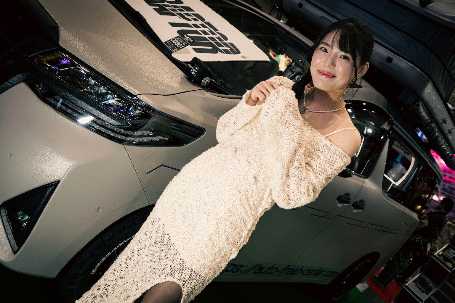 Une femme en robe blanche se tient devant une voiture
