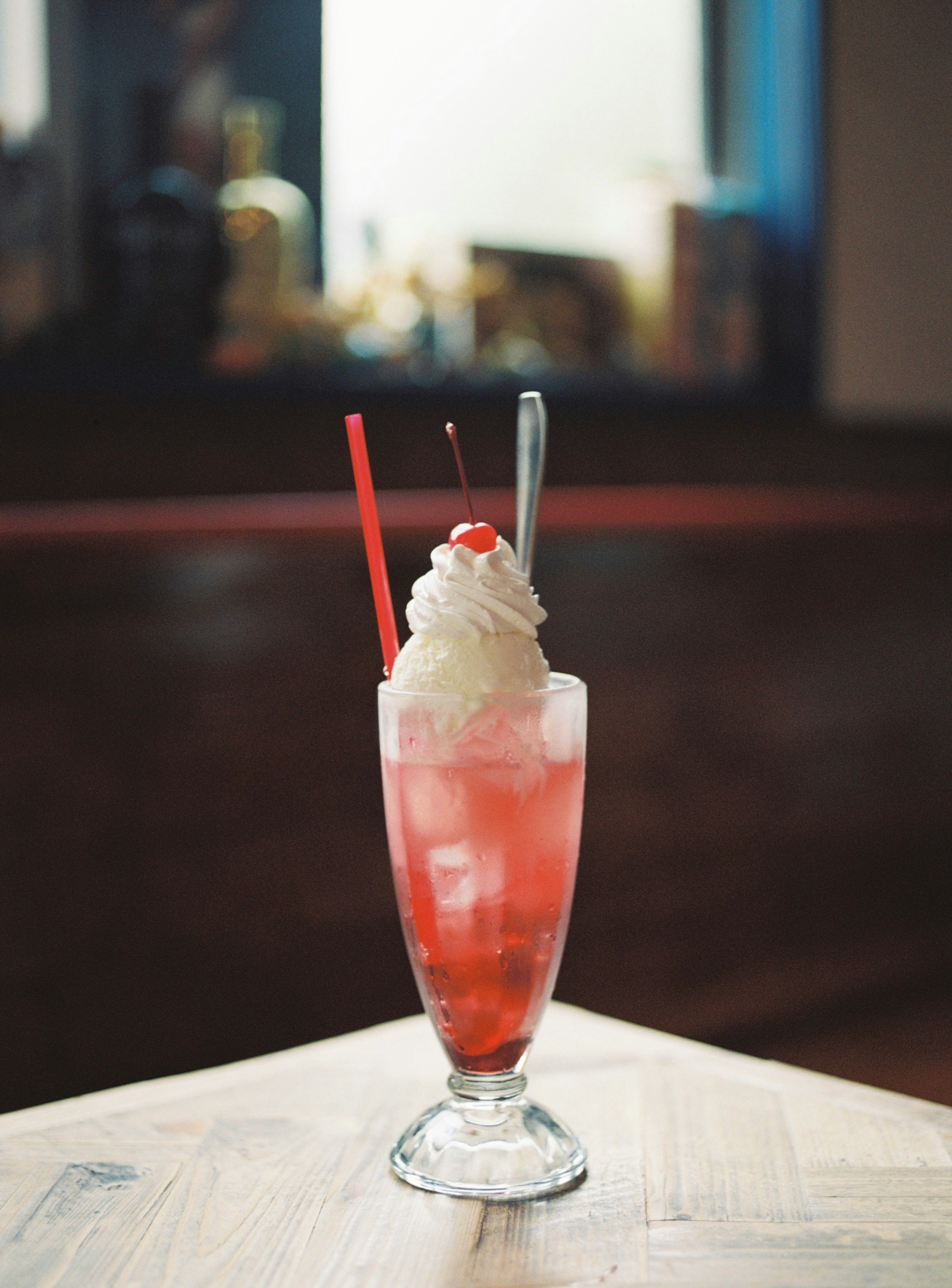red cocktail in a glass with a straw on an indoor table