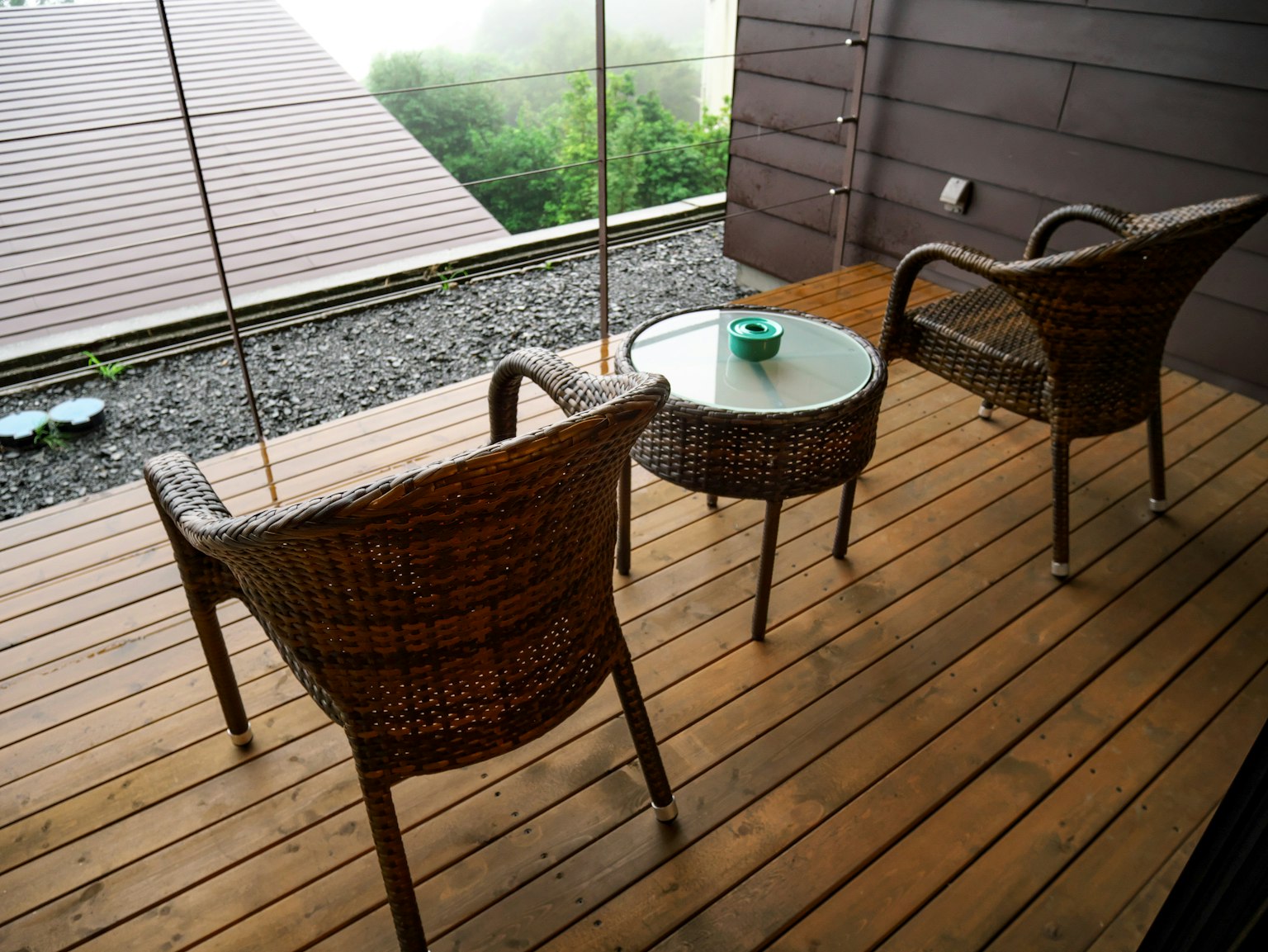 Zwei Rattanstühle und ein Glastisch auf einer Holzterrasse