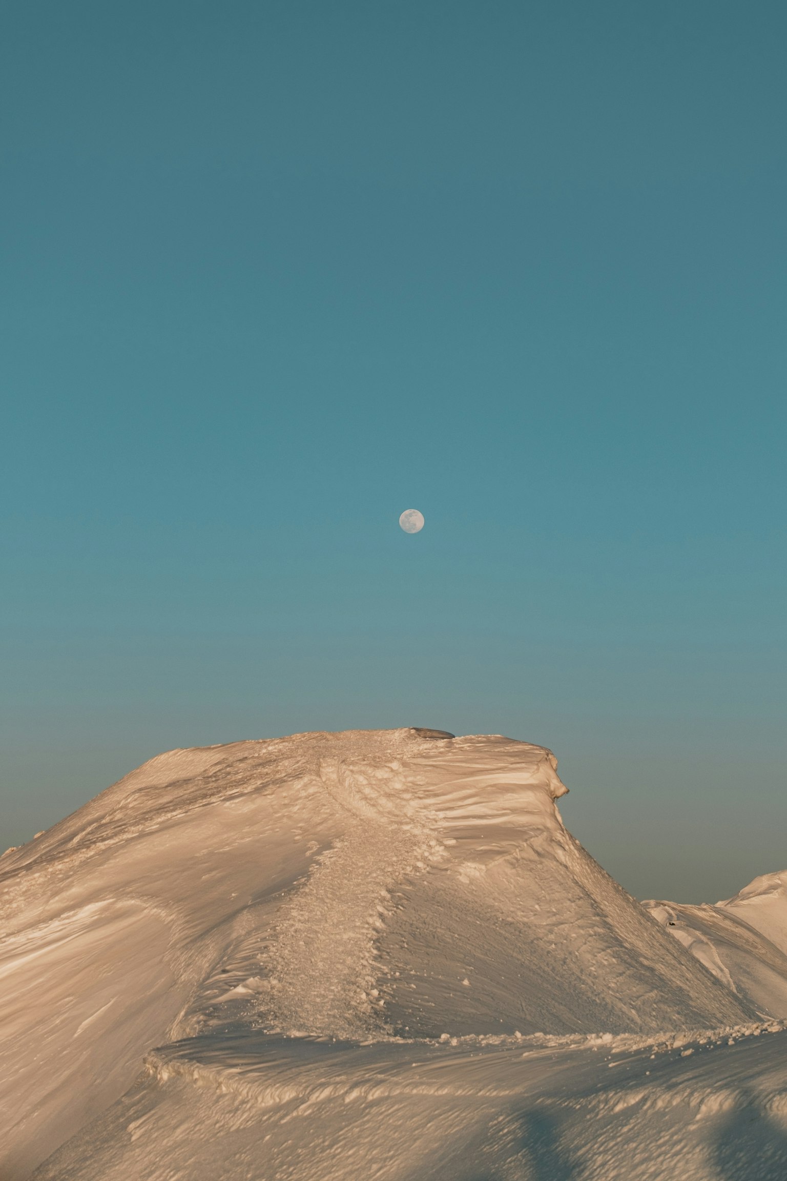 Montagna innevata con una luna in un cielo azzurro