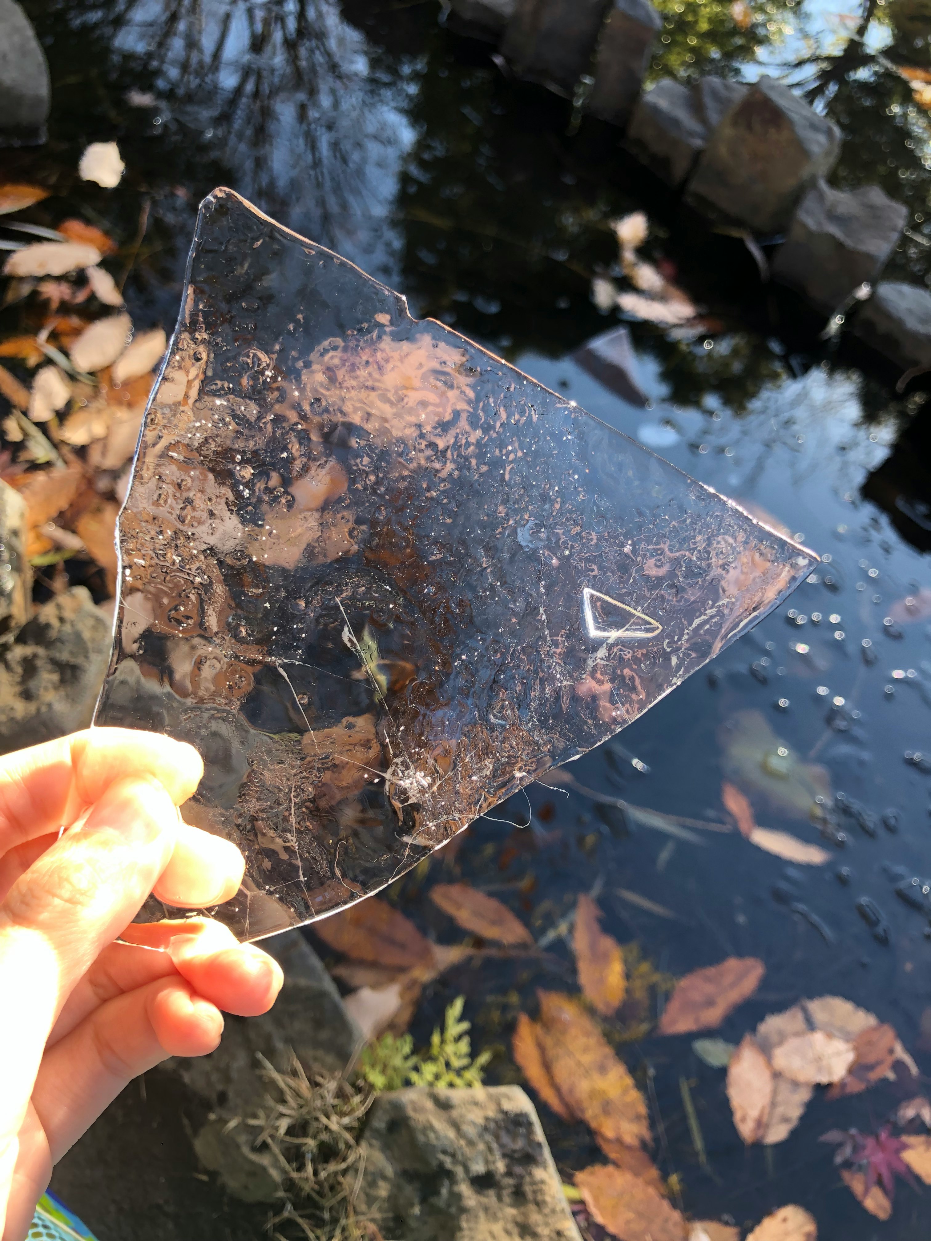 手持透明三角形玻璃碎片與水面倒影