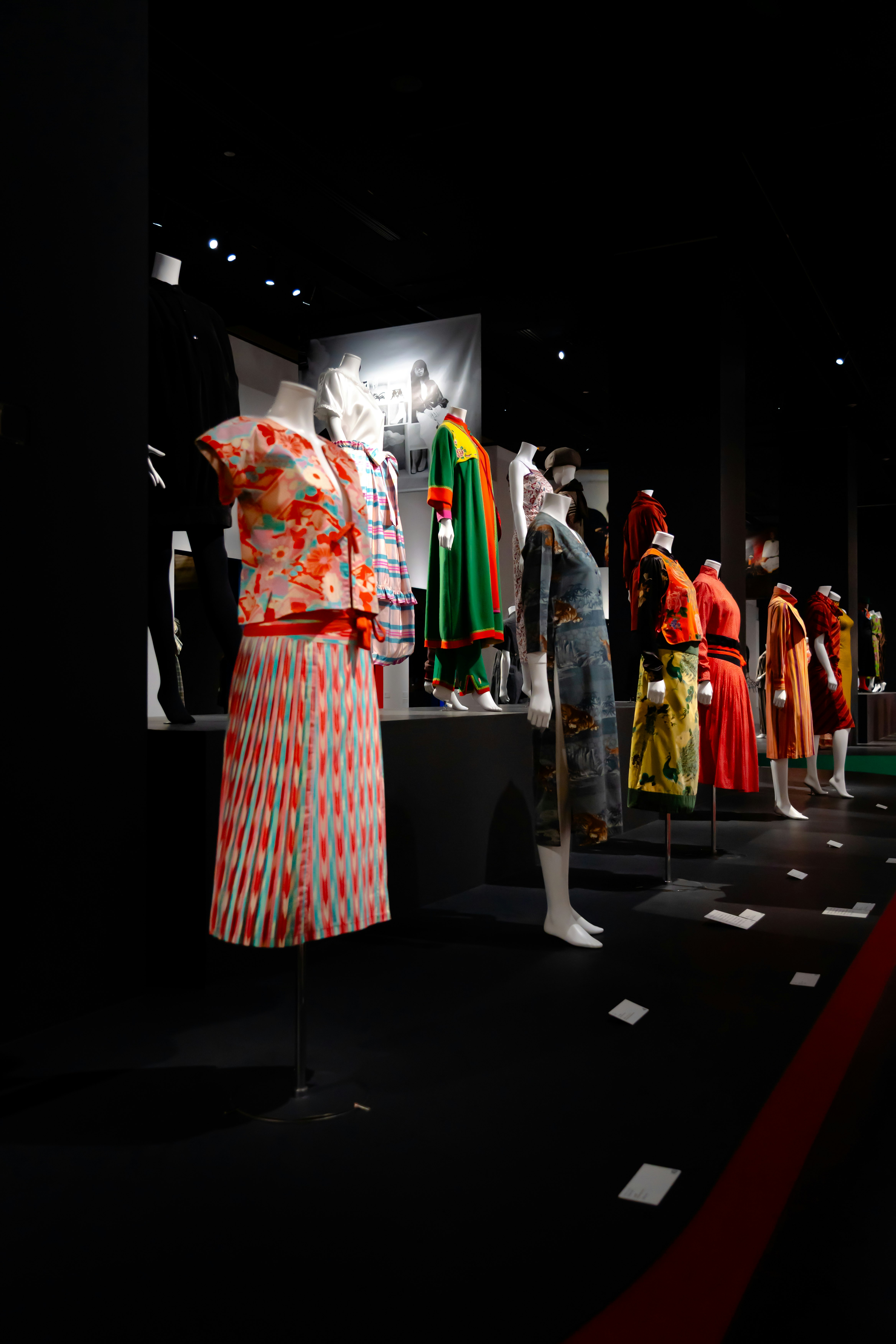 mannequins vêtus de tenues colorées dans un espace d’exposition sombre