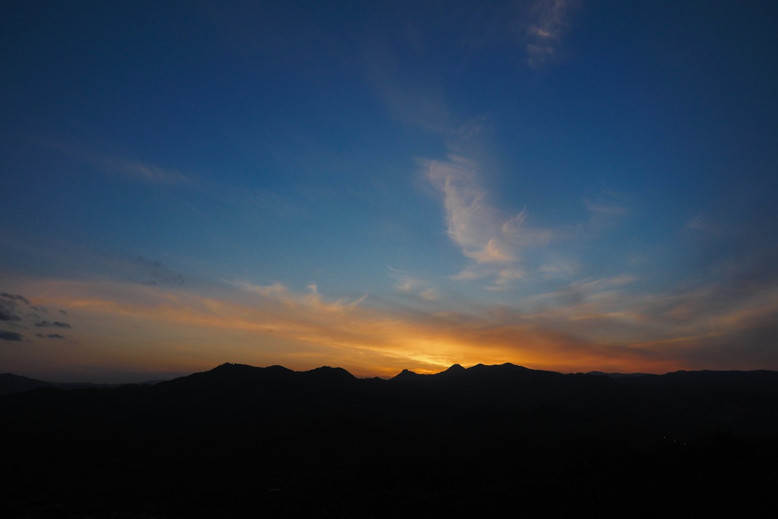 Silhouette de montagnes contre un ciel bleu avec un coucher de soleil vibrant