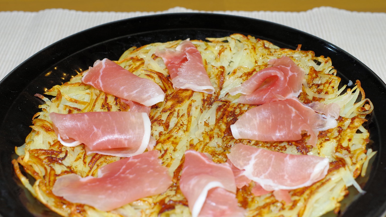 Un piatto di hash browns guarnito con fette di prosciutto