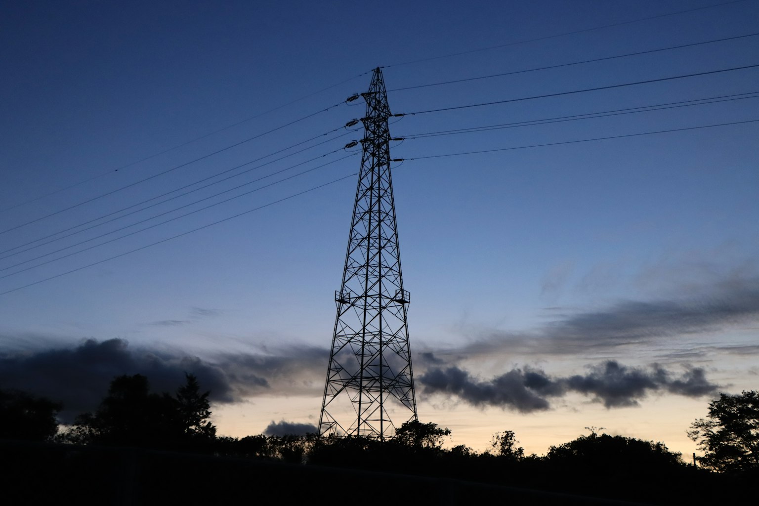 Silhouette di una torre elettrica e linee elettriche contro un cielo al crepuscolo