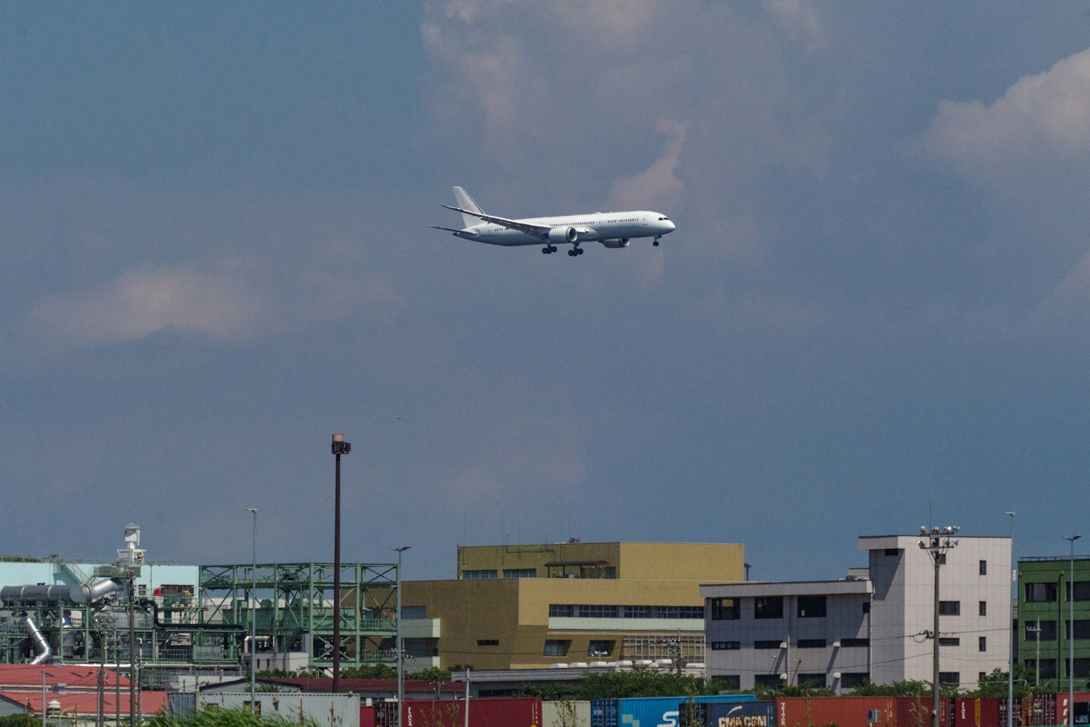 Aereo passeggeri in atterraggio vicino all'aeroporto con edifici e container in primo piano