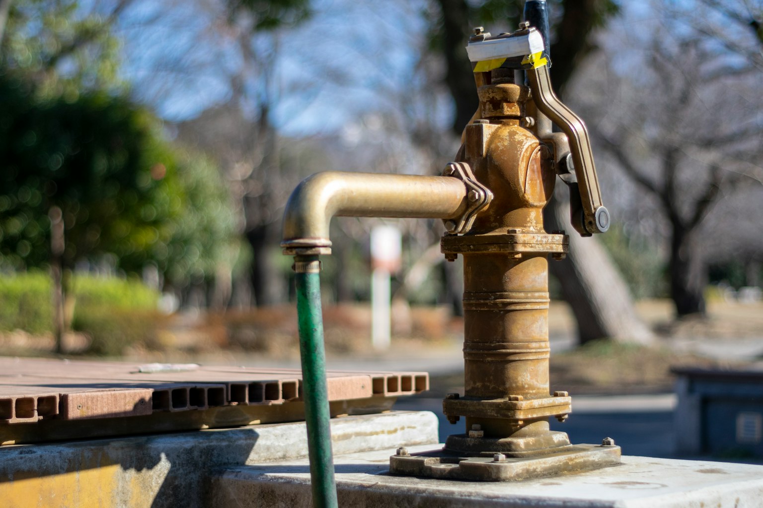 Una vieja bomba de agua de metal en un parque con una manguera verde adjunta