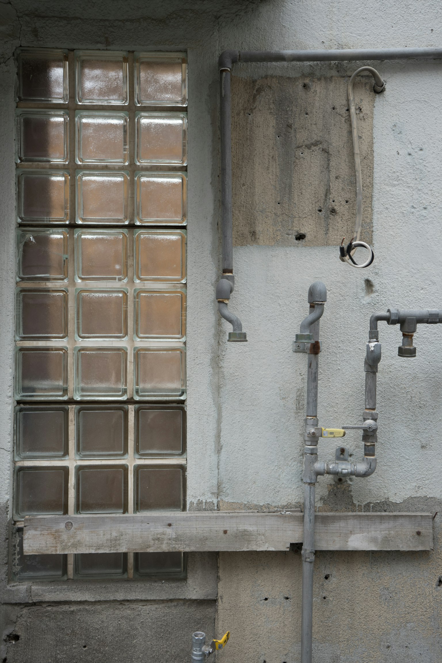 Glass block window with pipes and wooden panel on concrete wall